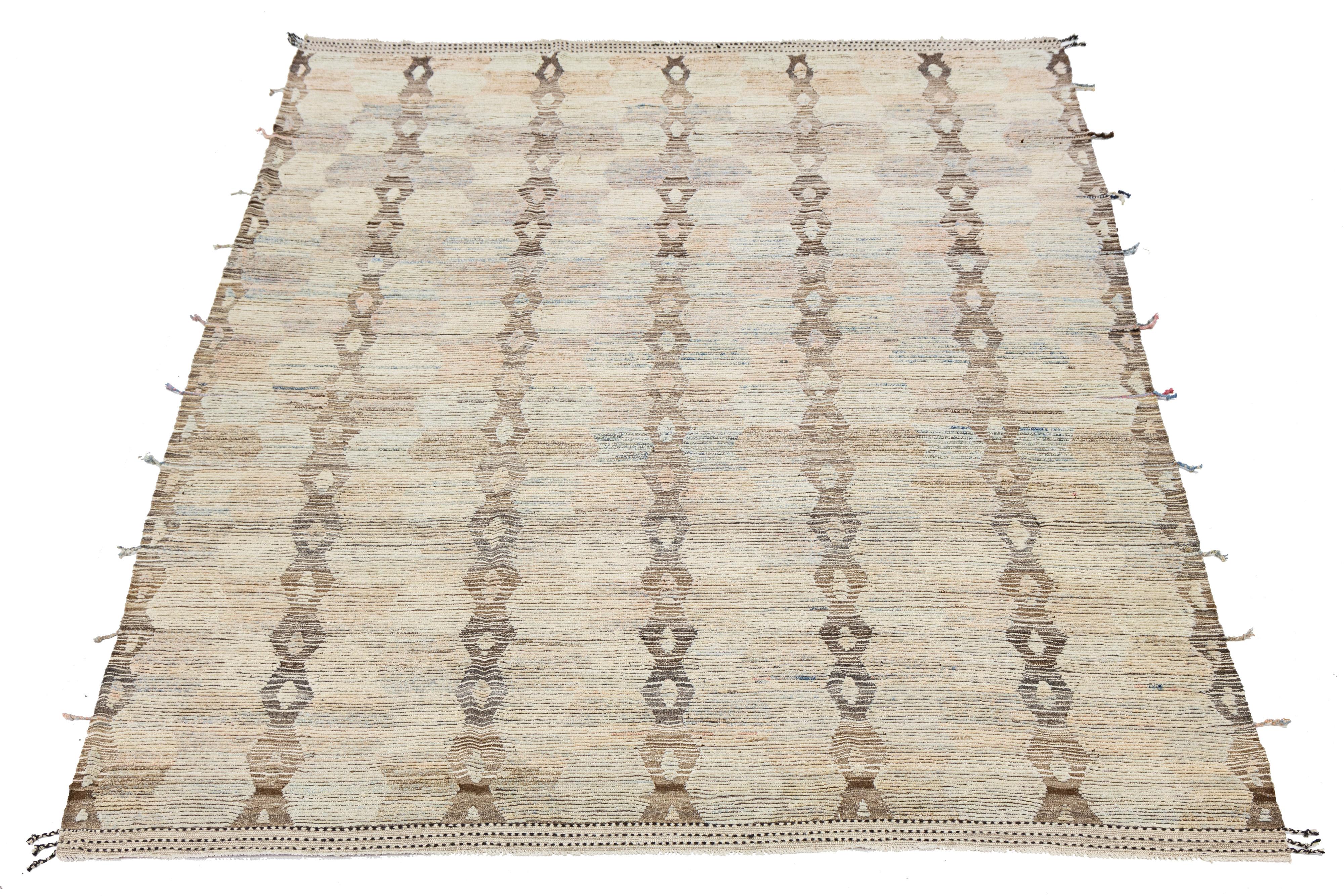 Dieser fein gearbeitete Wollteppich ist ein Beispiel für zeitgenössisches marokkanisches Design mit einem elegant gestalteten beigen Hintergrund. Die moderne Komposition besteht aus einer auffälligen Mischung aus Blau, Orange und Braun, die einen