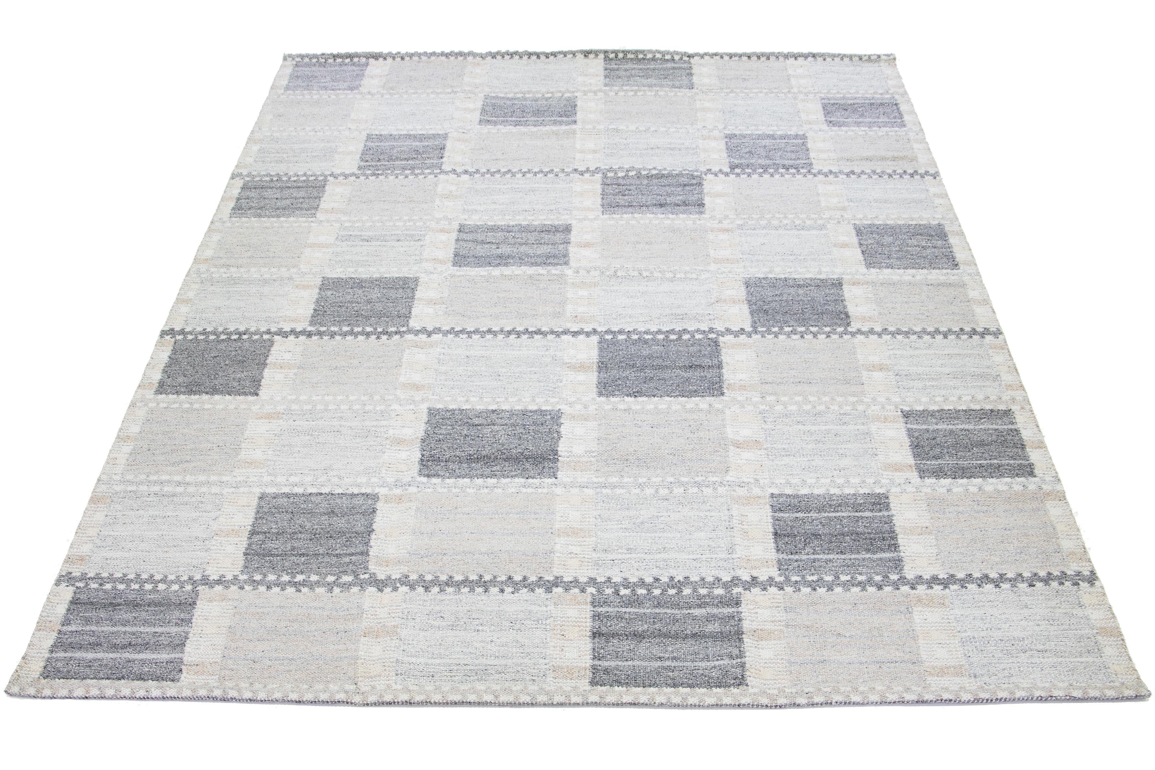 Inspired by Swedish design, this modern woolen rug features a subtle light gray backdrop. This exquisite flatweave rug is beautifully embellished with a striking geometric pattern in dark gray and beige tones.

 This rug measures 9'10