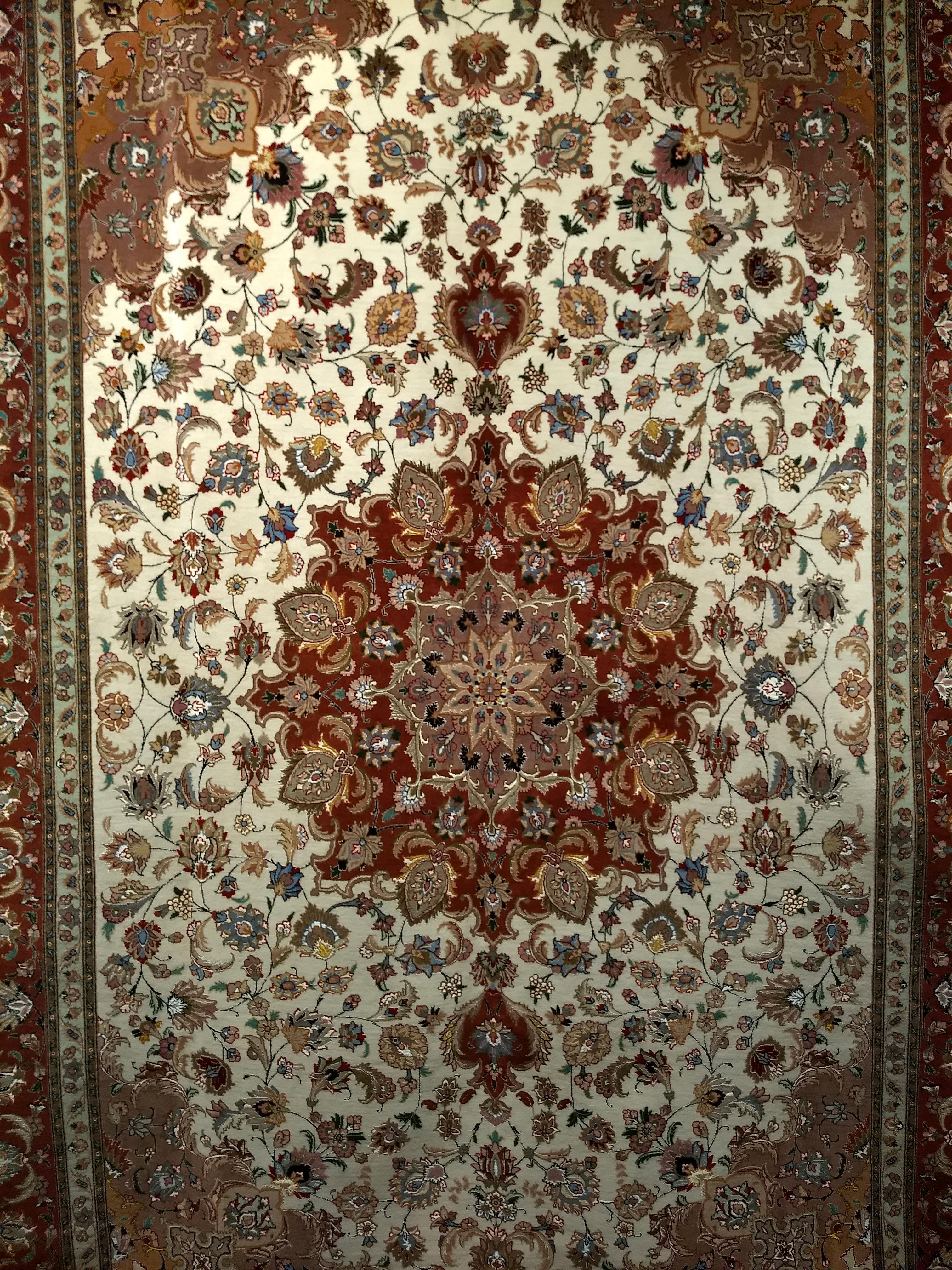 A beautiful finely woven room size Persian Tabriz in a floral pattern in primary colors of  ivory, chocolate and camel circa the late 1900s.   The rug has a wool pile with a cotton foundation and silk highlights throughout. The central medallion and