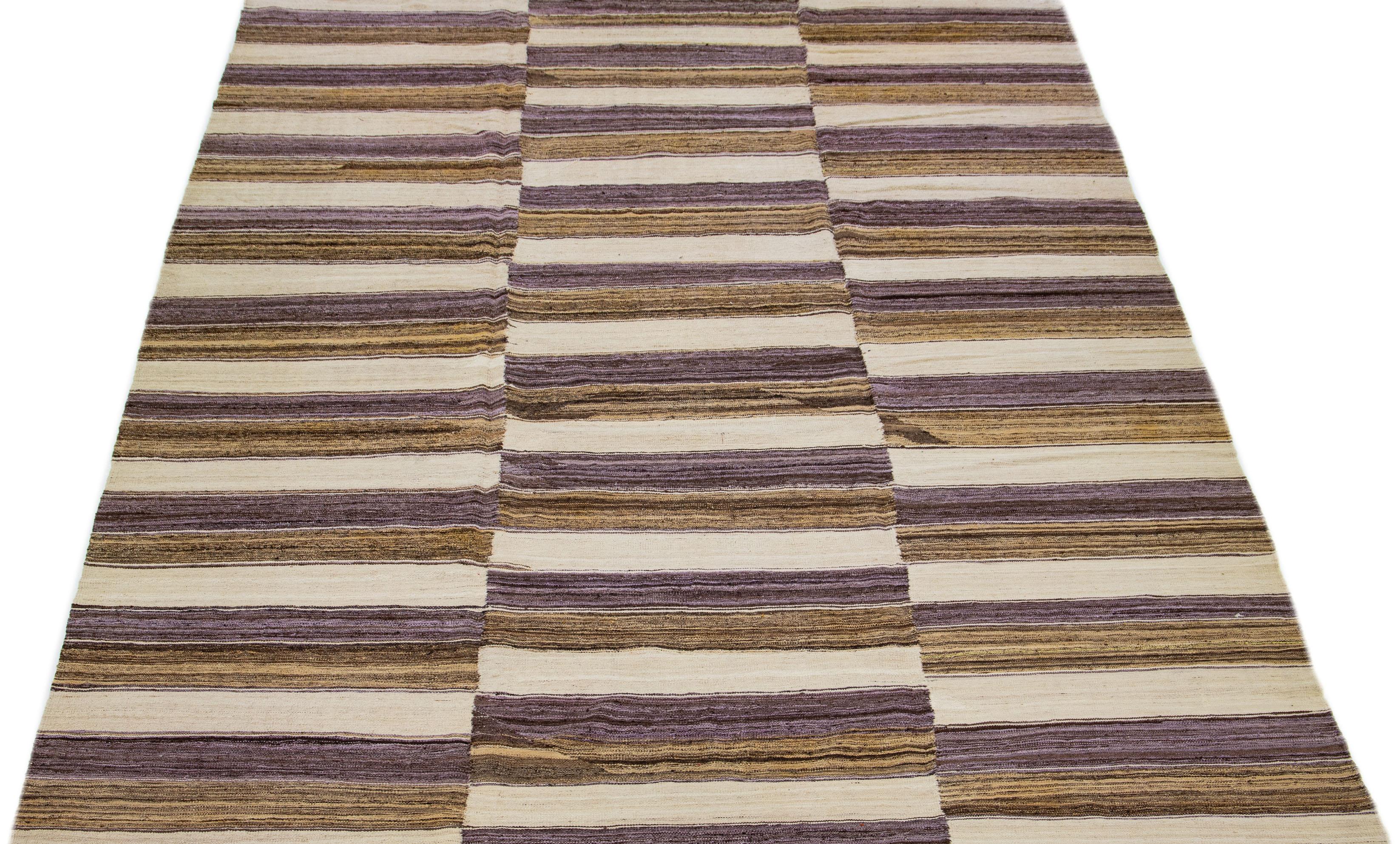 This contemporary kilim wool rug showcases a detailed and lively stripe design incorporating shades of beige, brown, and tan throughout.
This rug measures 10' x 13'10