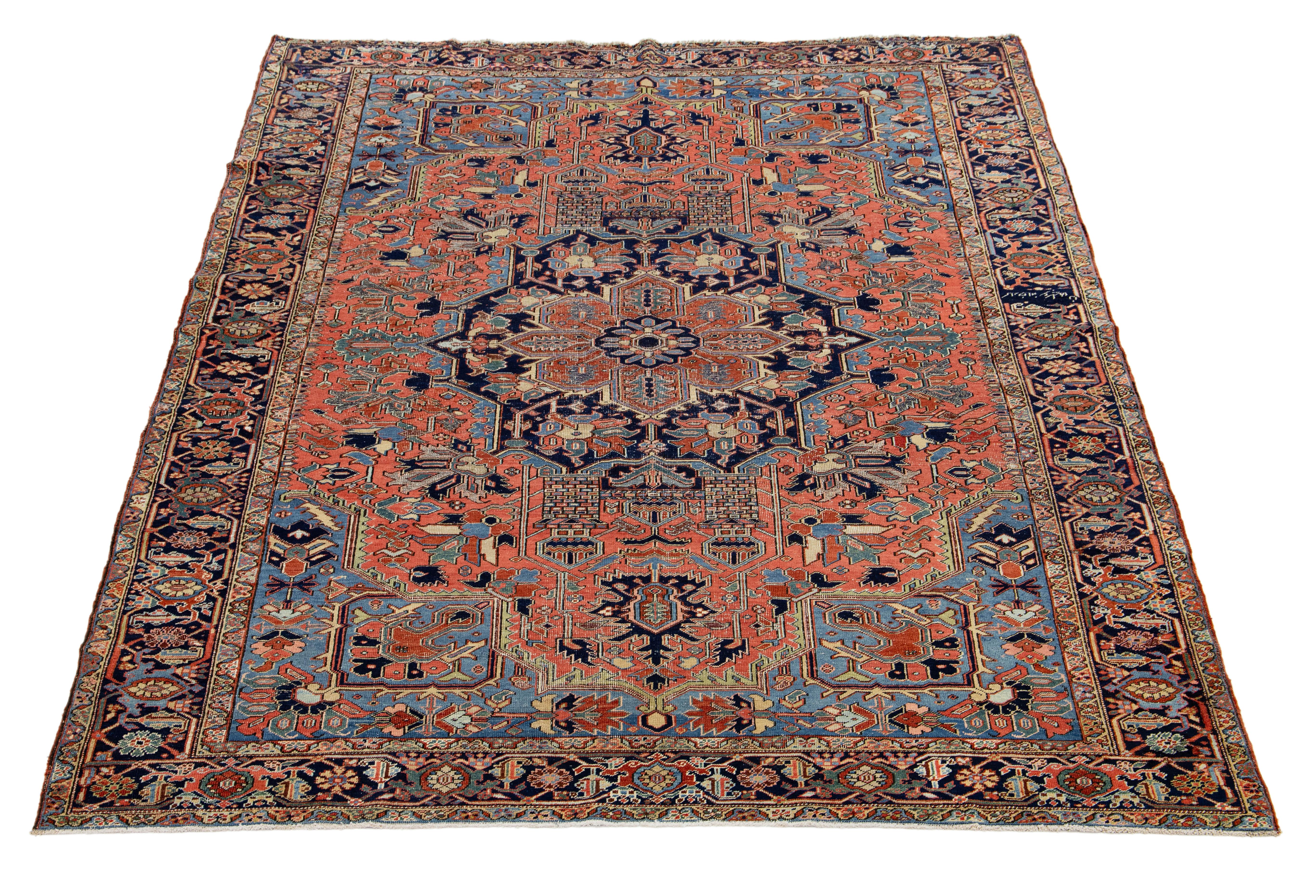 Discover the exquisite beauty of this antique hand-knotted Persian Heriz wool rug. Adorned with a vibrant array of colors against a rich red and blue backdrop, this stunning piece is sure to make a striking statement in any space. Elevate your home