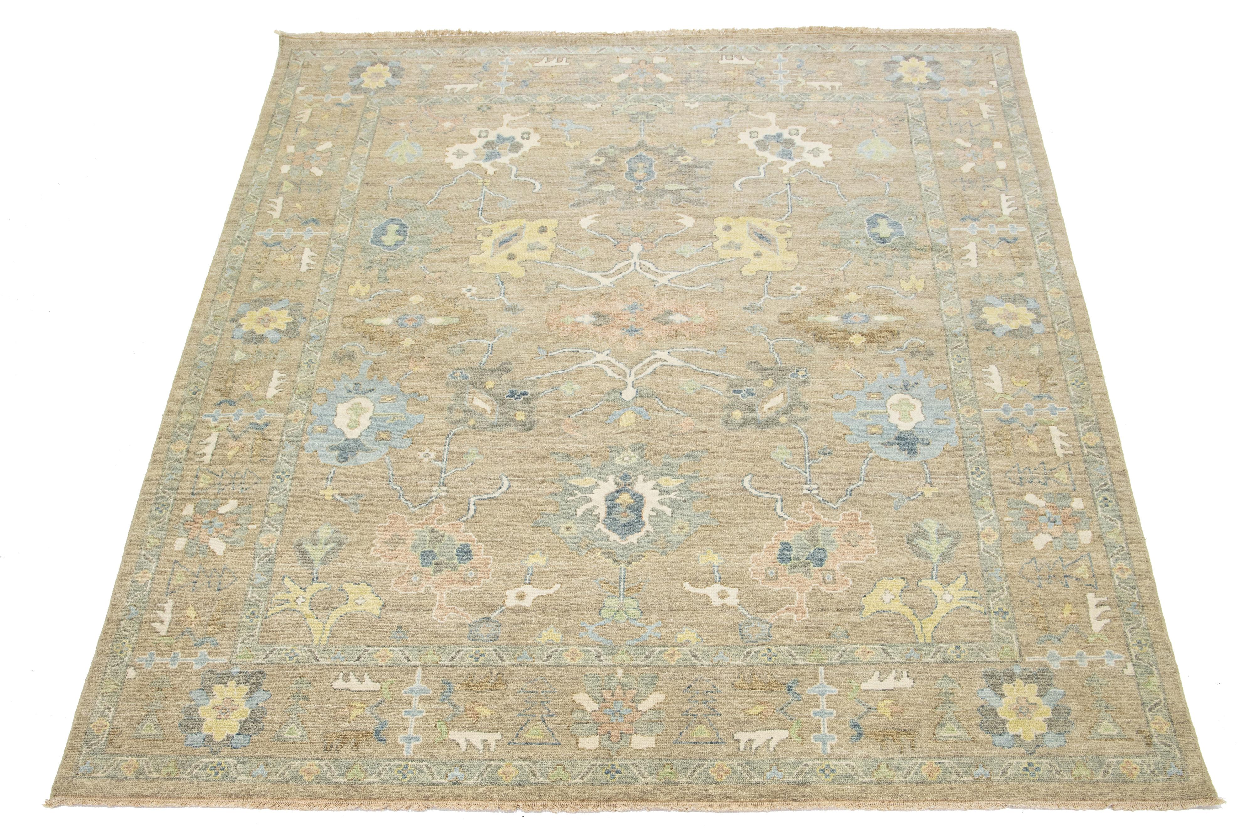 Dieser zeitgenössische Wollteppich im Oushak-Stil verbindet auf wunderbare Weise modernes Design mit dem zeitlosen Charme der traditionellen Oushak-Handwerkskunst. Der auffällige hellbraune Hintergrund ist mit lebhaften Blumenmustern verziert, die