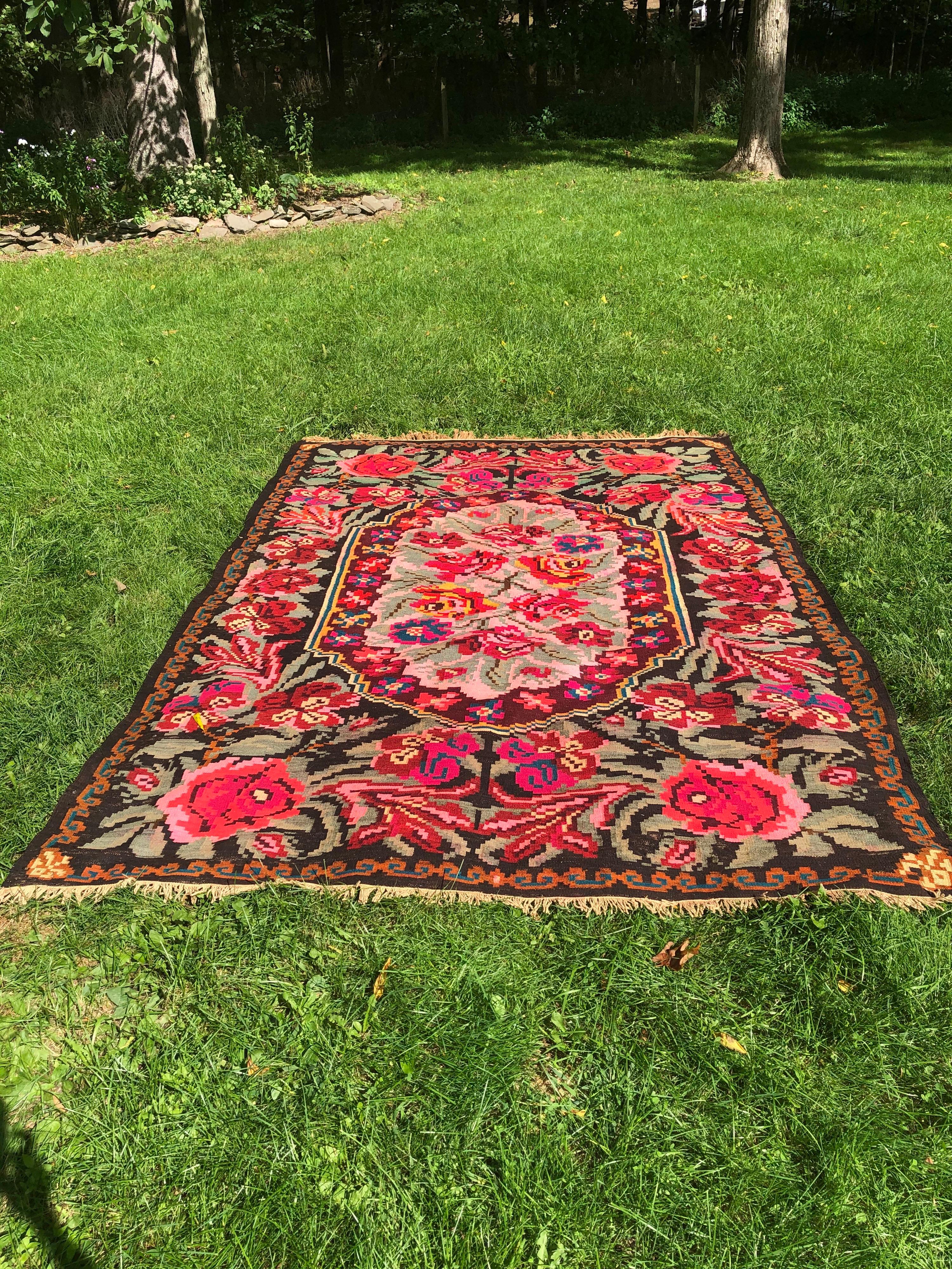 Overblown roses and other flowers adorn this room sized Kilim carpet. Floral medallion in the center. Lovely shades of red, pink and green on a black ground. Fringe in perfect condition. Carpet like new.