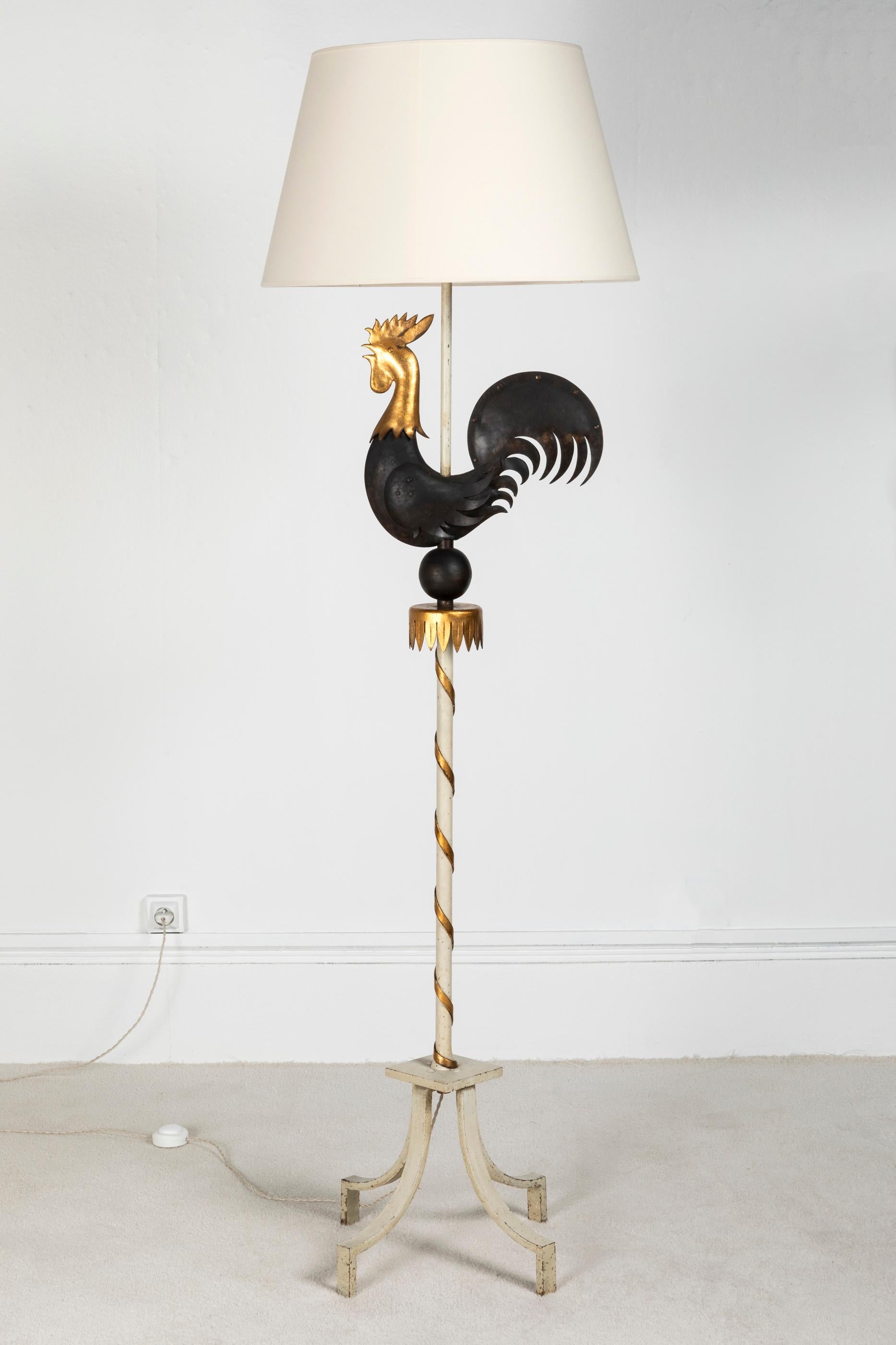 Un coq patiné en fer forgé noir et doré, le pied de lampe est laqué en blanc avec une spirale dorée autour. Cette lampe est dans le style et rappelle le célèbre ferronnier d'art français Gilbert Poillerat.