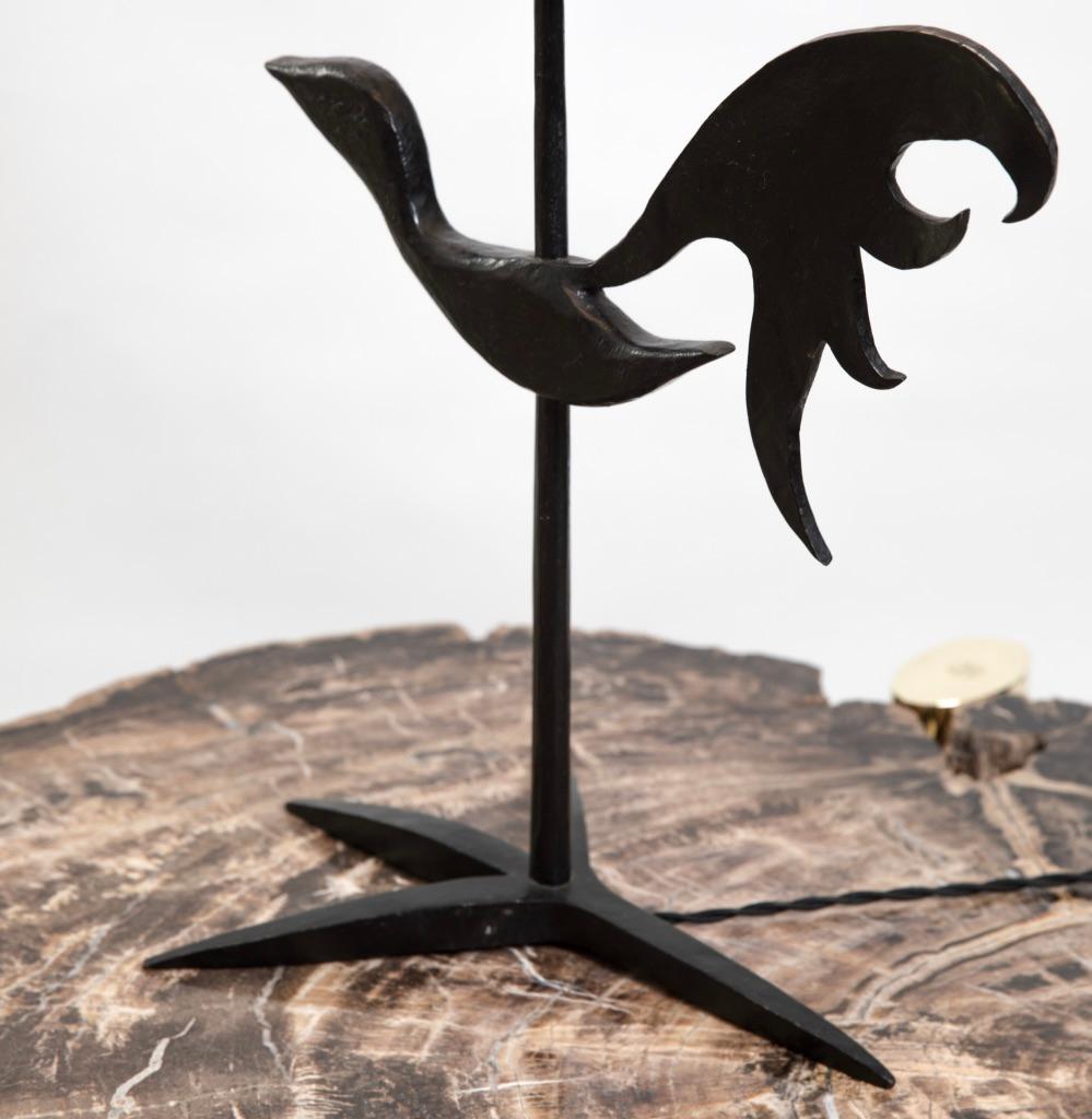 This table lamp from French sculpter Jean Touret is crafted from blackened bronze in the Brutalist style for which he is so well known. The bronze frame of the lamp sits on a foot in the shape of The Claw of a rooster. 
The shade is a burlap canvas