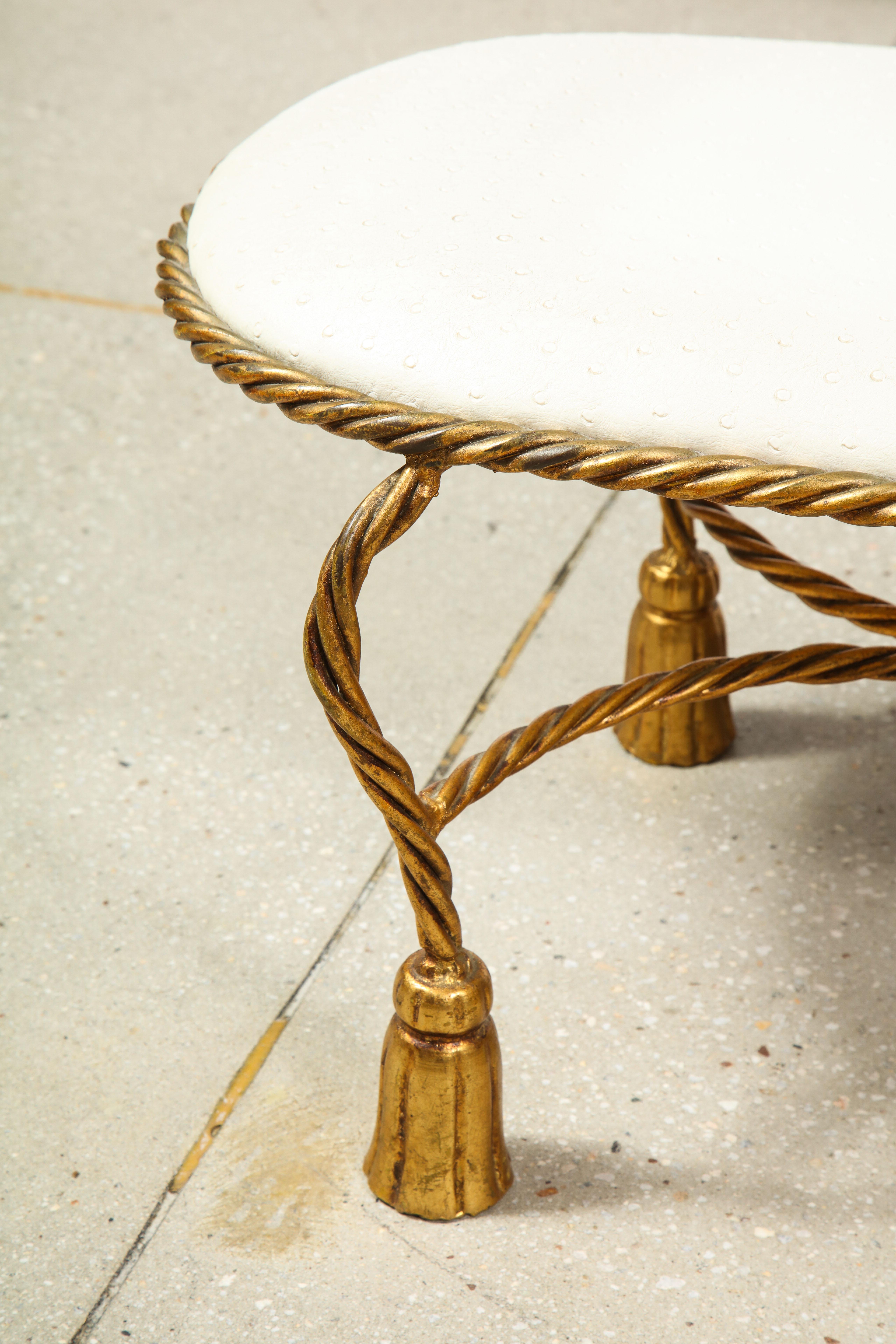 The white ostrich upholstered oval gilt metal bench supported by six rope and tassel legs and two cross stretchers.