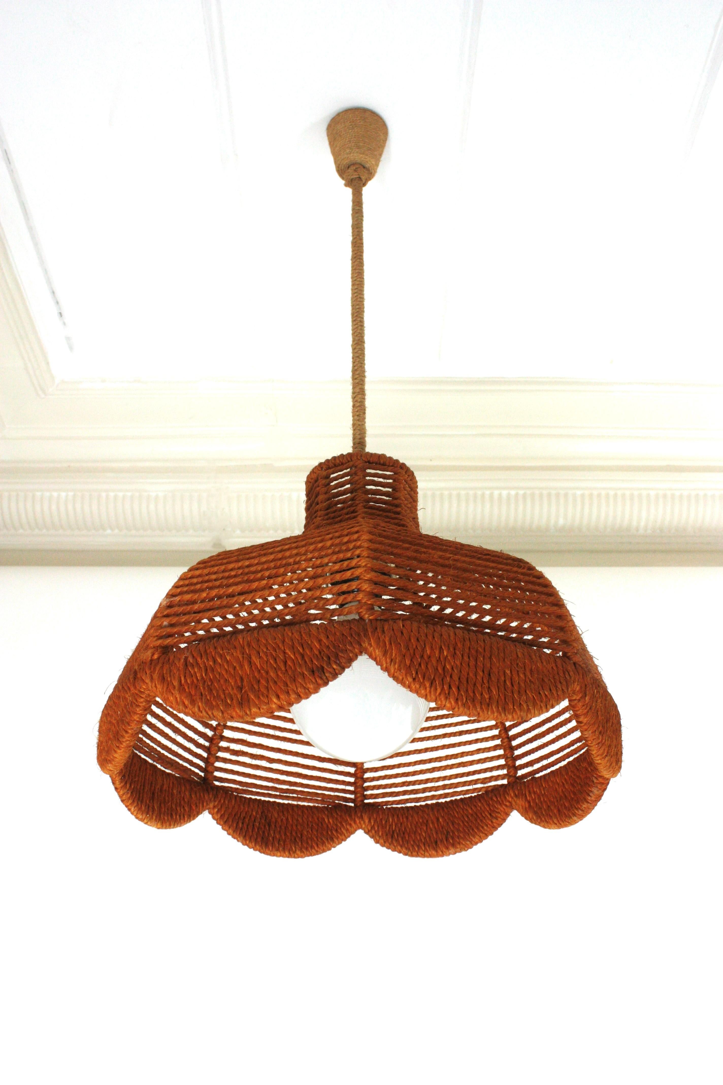 Eye-catching umbrella bell shaped rope pendant light with scalloped bottom, Spain, 1960s
This midcentury suspension lamp features an umbrella bell shaped rope covered lampshade in ginger color with an scalloped bottom. It hangs from a wire wraped