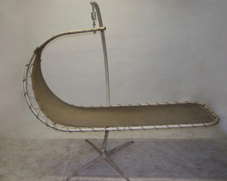 Sled-shaped swing chair with a tubular metal frame with original white enamel and the original stretched, thick linen seat supported by rope strung around the frame through grommets.