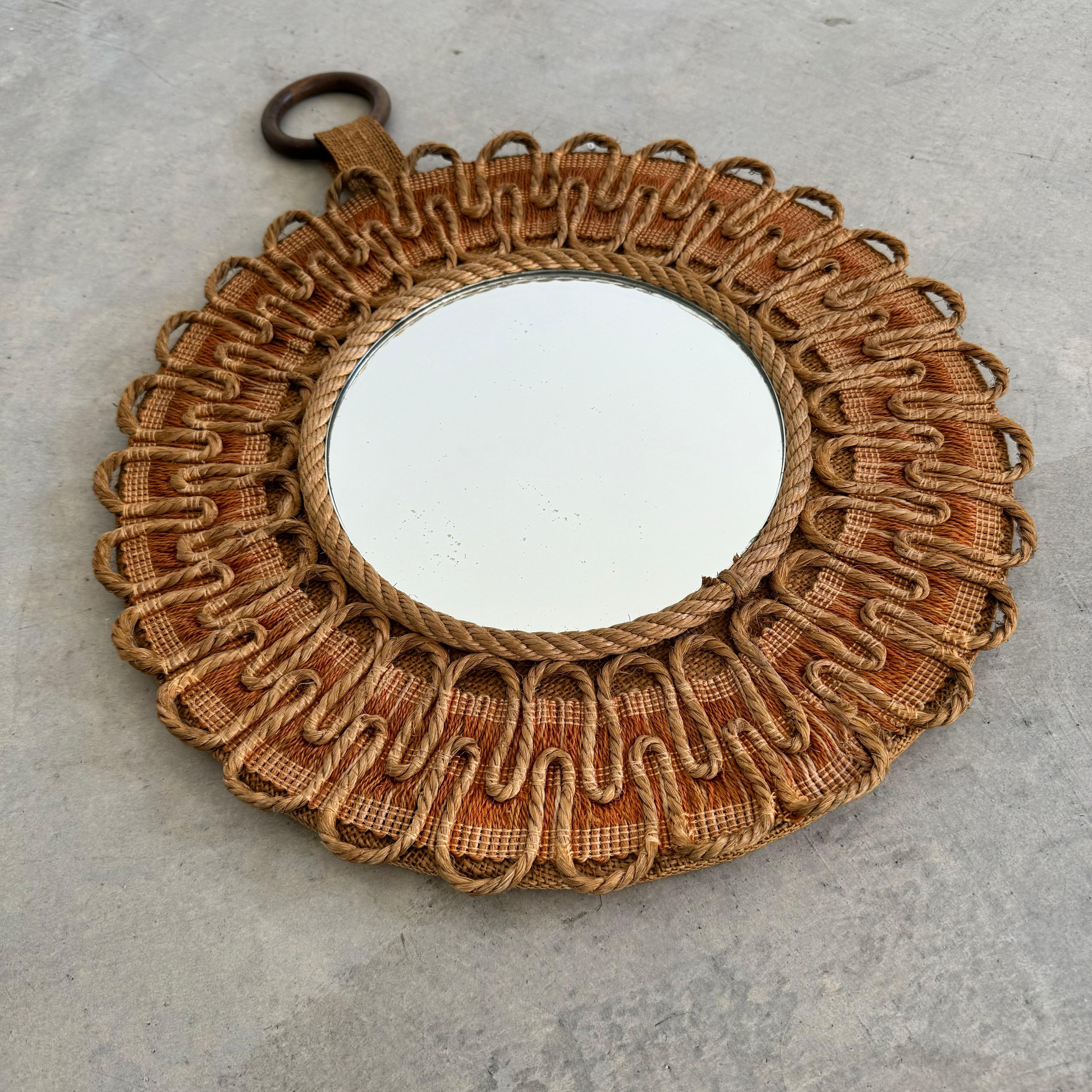 Gorgeous circular mirror made in France, circa 1950s. In the style of Audoux Minet. Undulating rope loops surround the outer frame of the mirror with a braided rope band immediately surrounding the glass. Hanging tab with circular wooden ring for