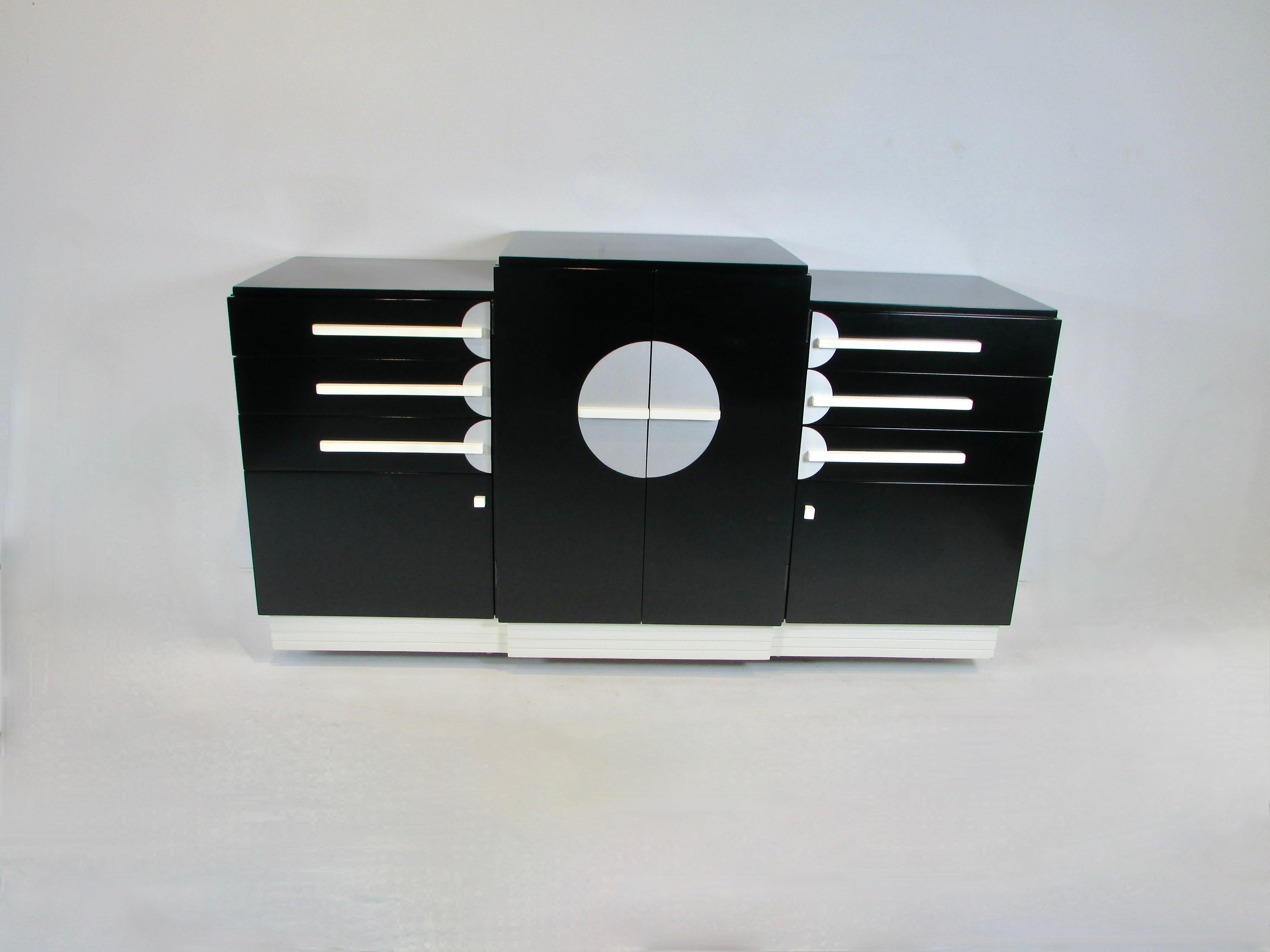 Period Art Deco credenza stepped form skyscraper style  in cream and matte black lacquer finish . Center section holds three shelves behind lacquered doors with white pulls mounted on round aluminum motifs . Either side cabinets have  three drawers