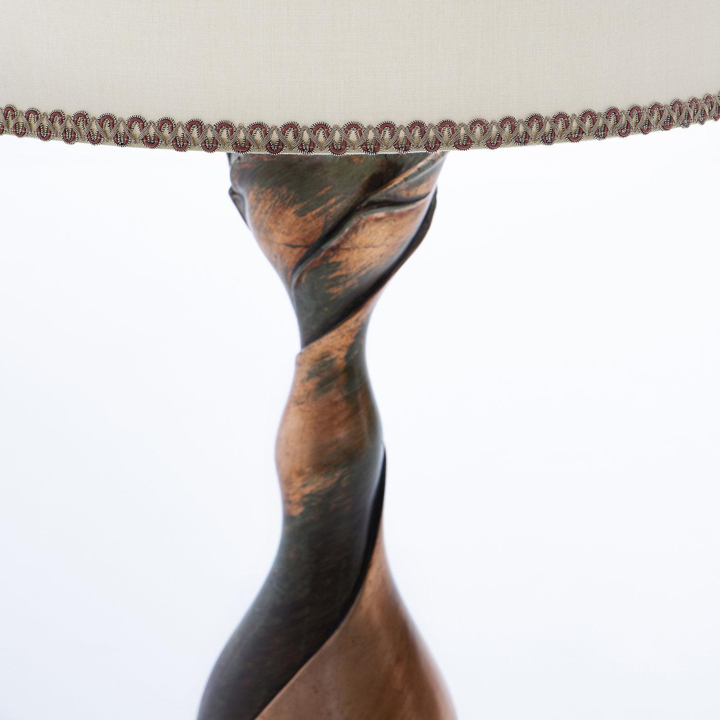 The ephemeral beauty of flowers is conveyed in the finely rendered solid wood base in this sculptural table lamp. Entirely covered in copper leaf boasting a satin and antiqued finish, the slender support for the lampshade gracefully stems from a