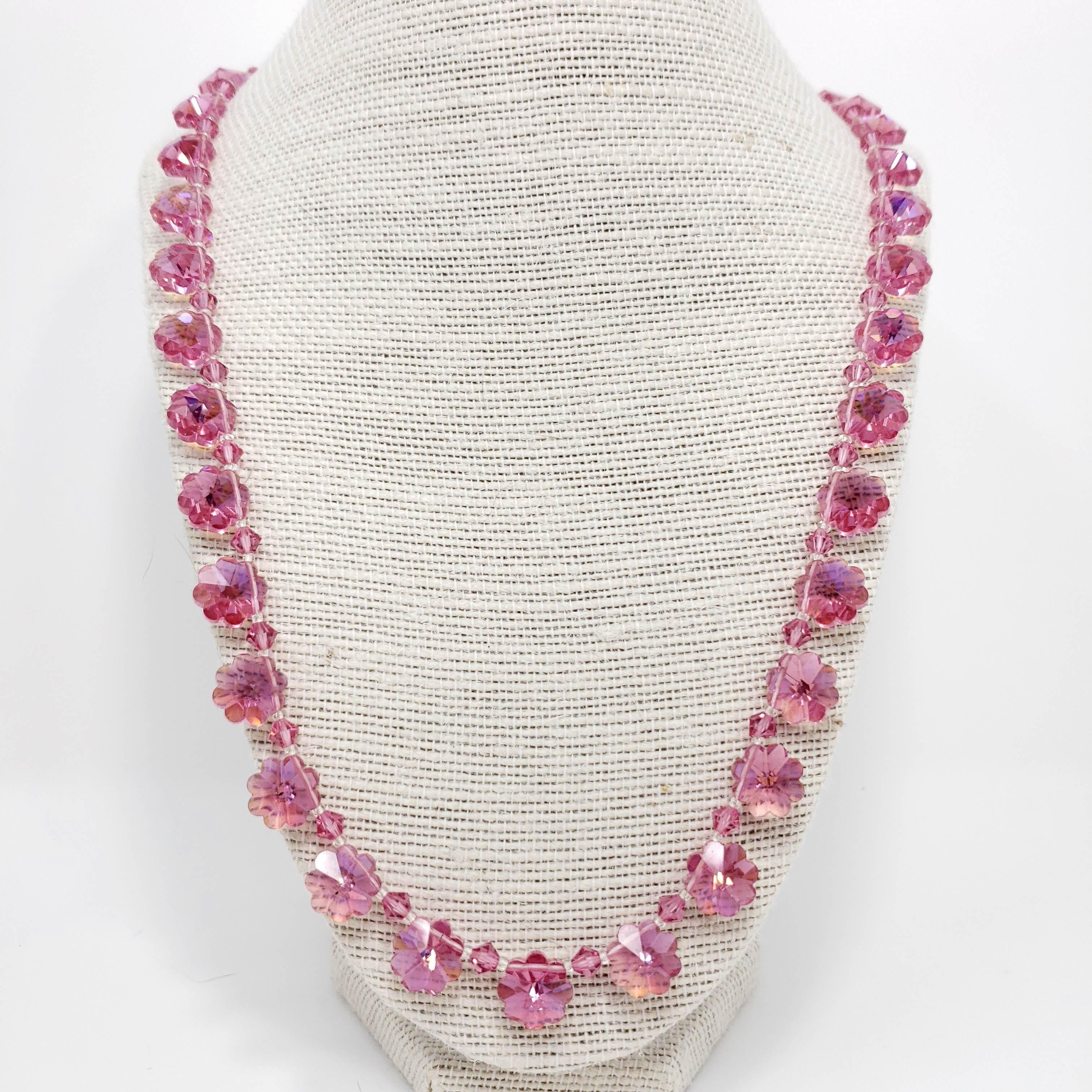 A rose-colored necklace with flower-shaped crystal beads, with a glowing aurora borealis tint on one side of each bead. Gold tone box-style clasp.

Estimated date mid 1900s.