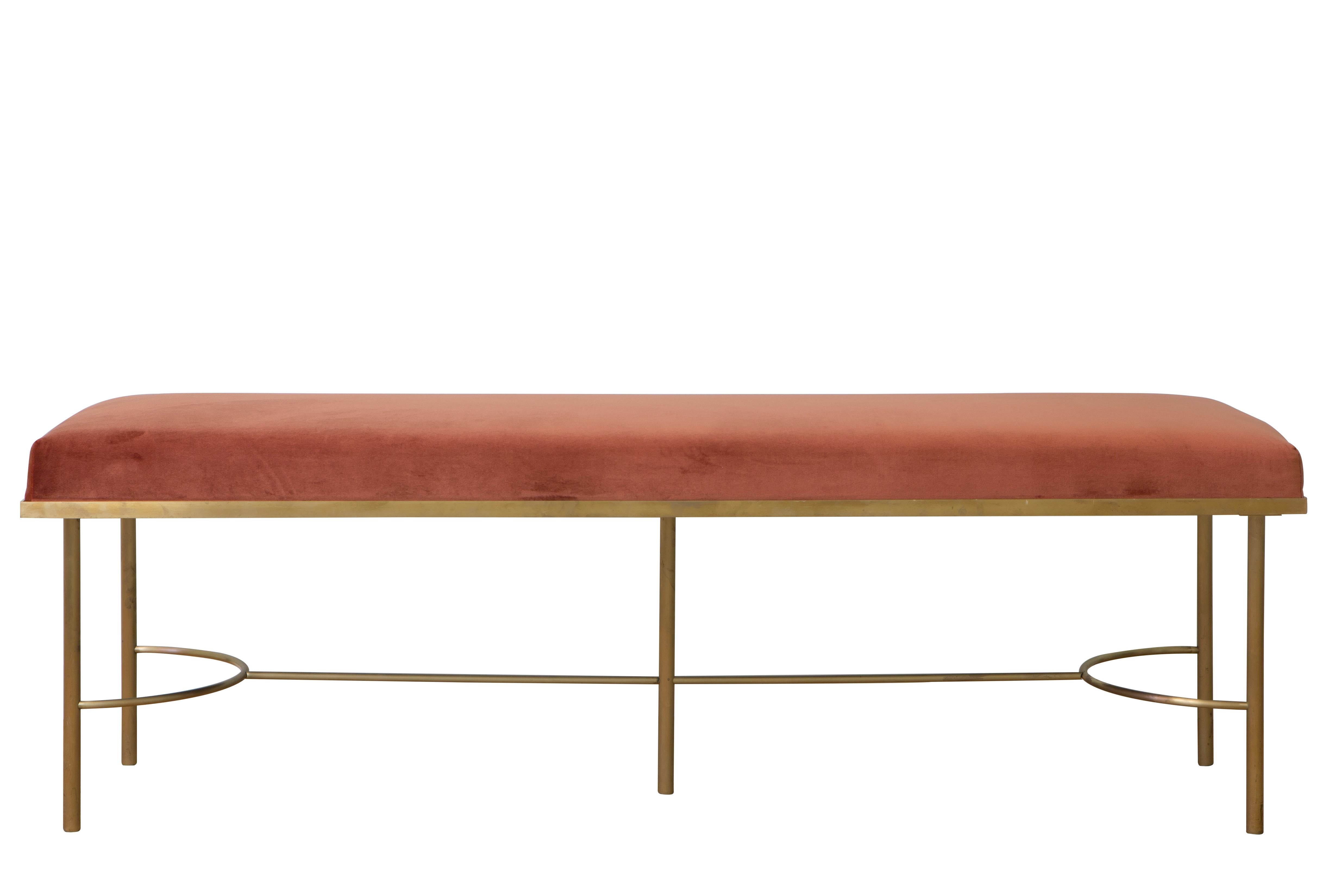 This sophisticated bench features a generous cushion that is upholstered in rich cotton velvet with a charming coral color and supported by a delicate brass frame made up of five legs connected by a lower element that mixes curves and straight