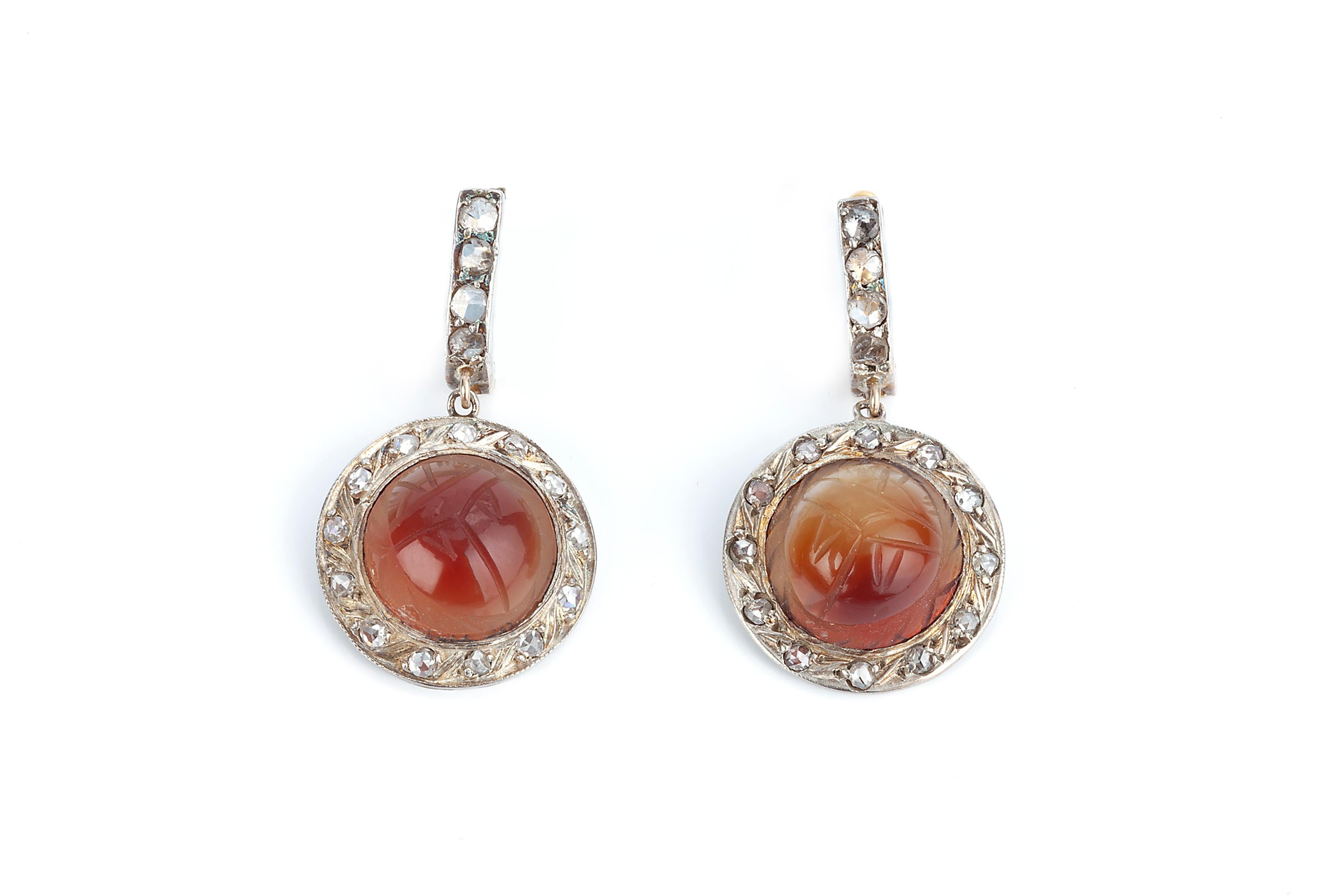 A pair of rose cut diamond and carved carnelian scarab beetle earrings.  The Central carved stone is set around a boarder of rose cut diamonds set in silver and gold overlay. There are maker marks on the back of the stones or date marks. The