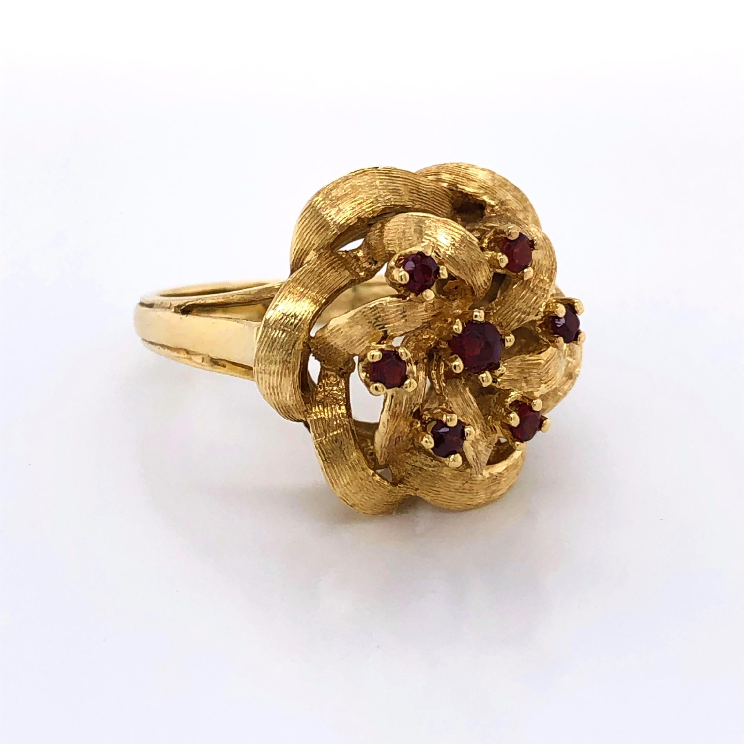 Twists of twelve karat yellow gold create the floral head of this lovely cocktail ring. The ribbon like petals formed by the open filigree are adorned with rose cut ruby gemstones, .14 carat total weight. In ring size 7.5 and sizable. Gift boxed.

