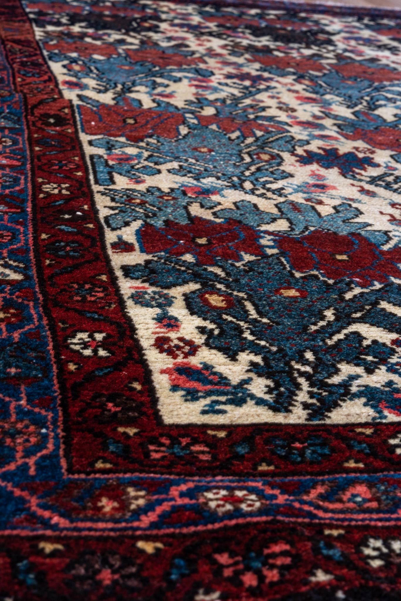 This is a beautiful Malayer rug measuring 3.3 x 4.9 feet. It features a repeating floral motif on a soft ivory field, complemented by rich accents of red, blue, and black. The intricate border frames the design, adding depth and character. Its fine