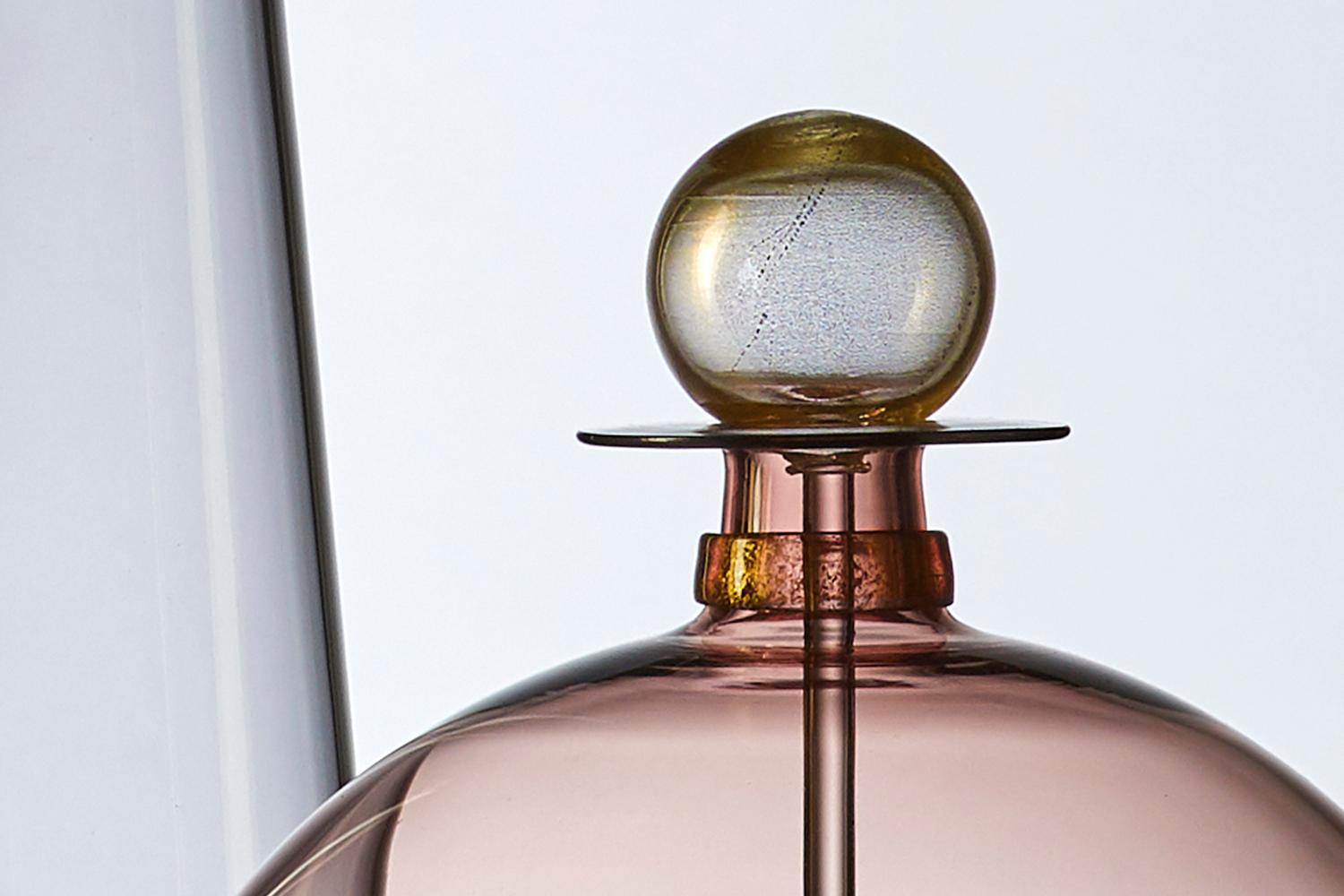 The modernist hand blown Jewel Bottle by Vetro Vero features rose tinted glass, and shimmering gold details. Inspired by apothecary collections and decanters of Mid-Century Modern design, the pink carafe makes a standalone statement or a stunning