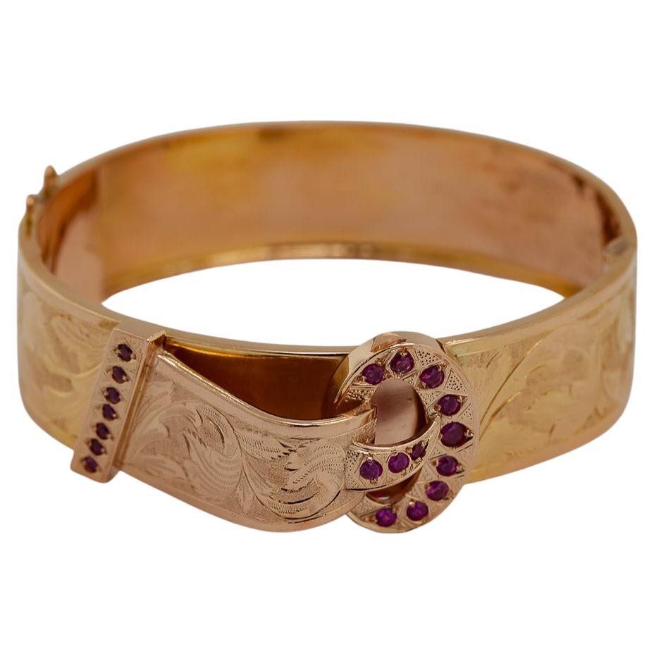 This beautifully hand engraved 19k rose gold buckle motif bangle, 
23 mm tapering to 17 mm,
Features (19) synthetic round-cut rubies, 
Portugal Porto hallmarks on tongue, 19.2 K, 
Circa 1938-1984, 
Gross Weight 33.27 grams, 
Internal diameters 65.7
