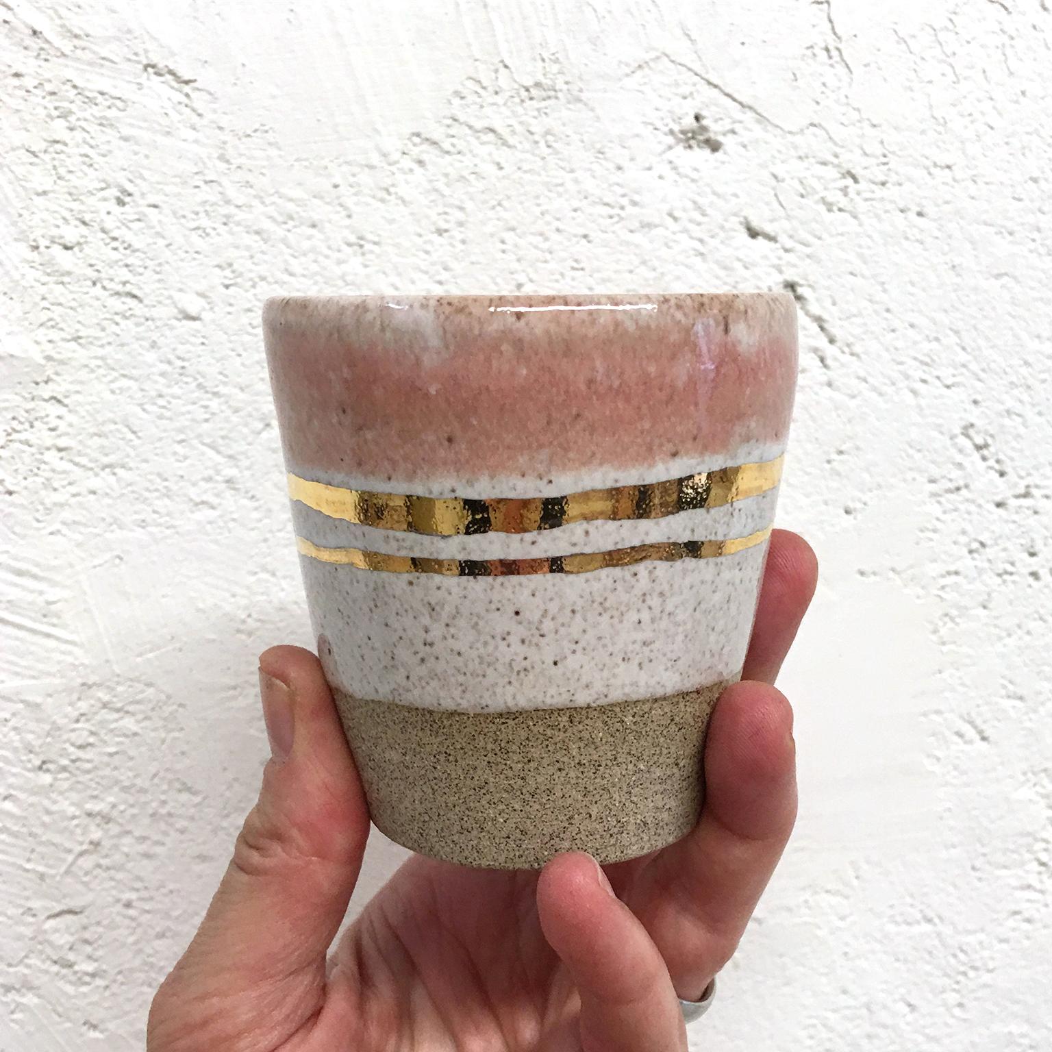 Kim Brown's lightly speckled stoneware cups are wheel thrown and glazed in white and rose with 22-karat gold luster stripes. Measuring approximately 3.25