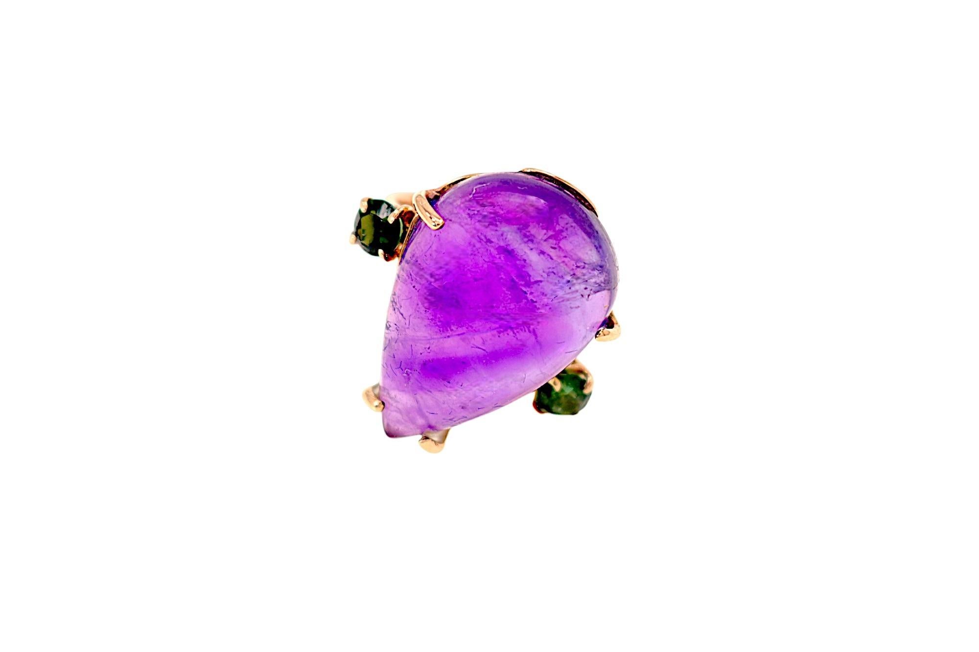 Anillo artesanal de oro rosa de 9 quilates con una gota de amatista talla cabujón, flanqueada por dos turmalinas verdes talla brillante. Las piedras están engastadas y montadas en una banda de oro macizo. Las dimensiones de la gota de amatista son