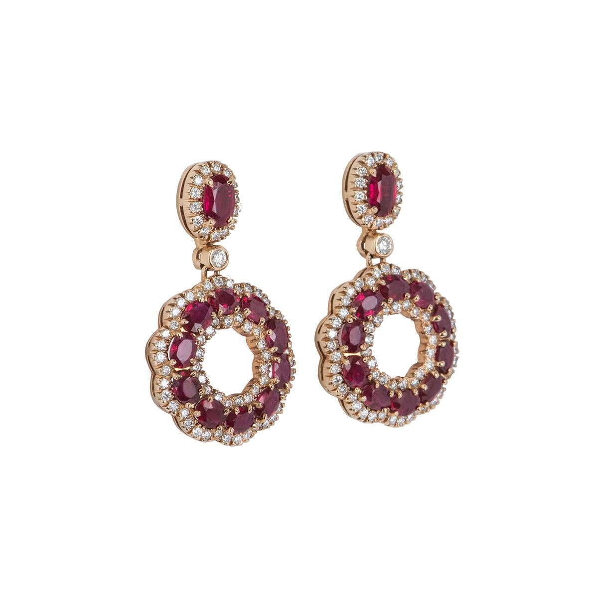 A stunning pair of 18k rose gold ruby and diamond earrings. The earrings feature a single ruby with pave set round brilliant cut diamonds around it followed by a single diamond, suspended from it is an open work circular motif set with oval shaped