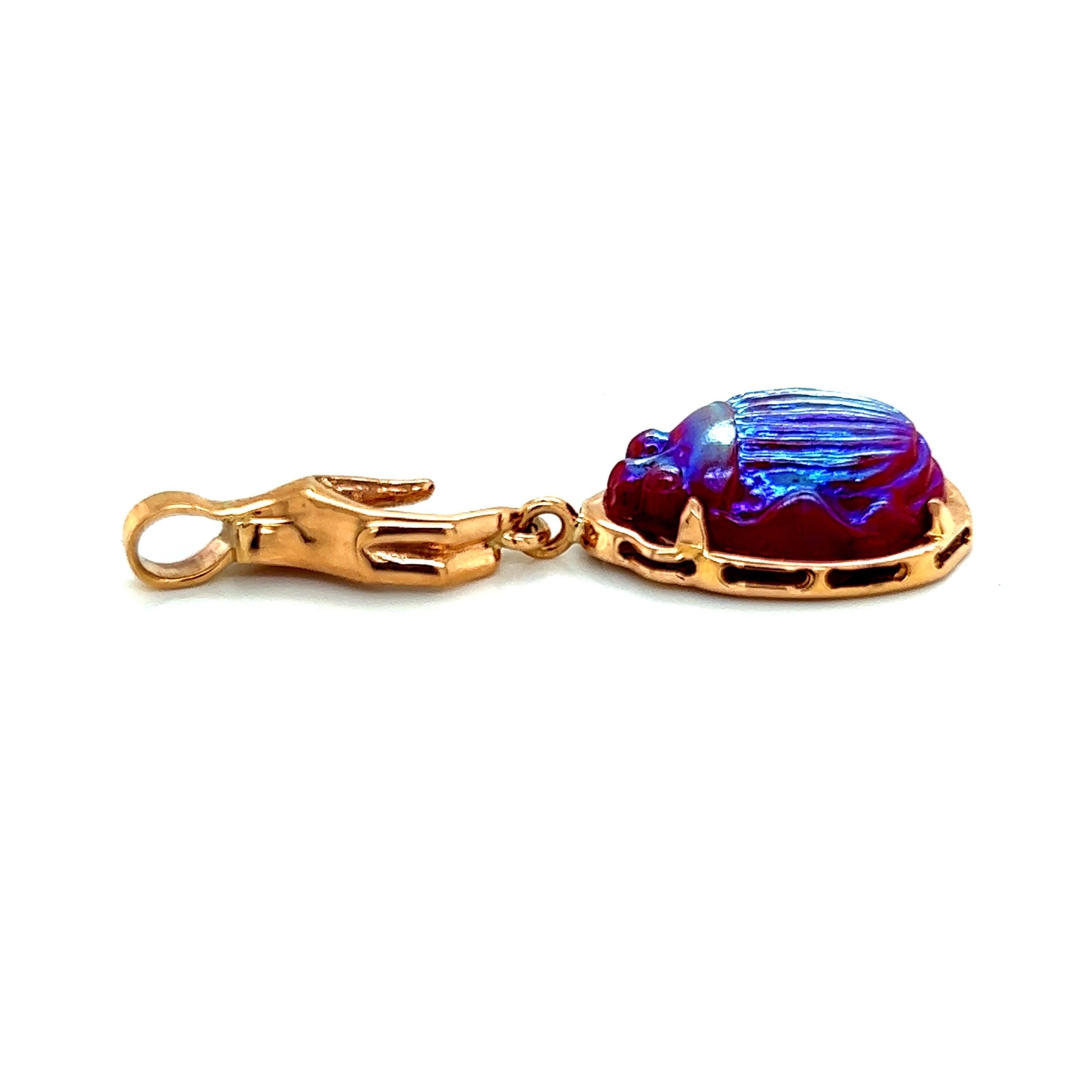 The 18k Pink Gold Pendant with a Hand holding a red iridescent vintage Tiffany glass scarab is a truly unique and striking piece of jewelry. The pendant is crafted from high-quality 18 karat pink gold, giving it a warm and luxurious tone that