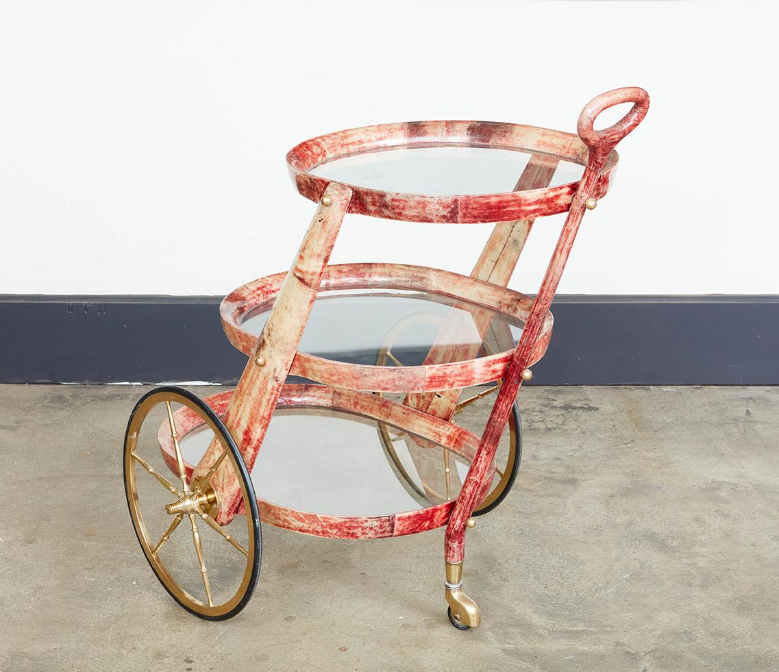 The rare rose color bar cart by Italian designer Aldo Tura. The three-tier cart on two brass wheels with a rear stand.The surface is covered with lacquered goatskin and highlighted with bronze medallion and ball hardware.

Handle Height: 35