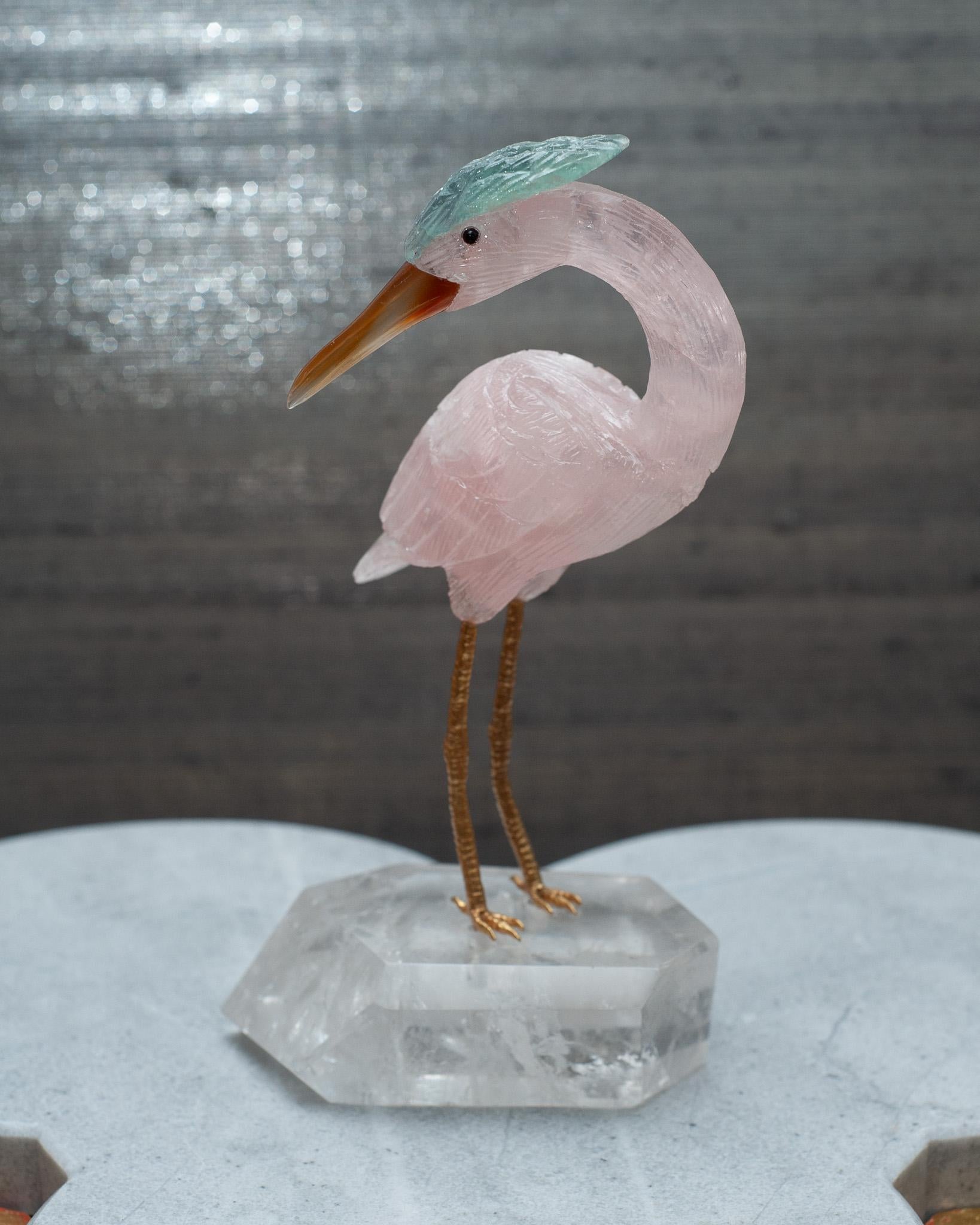 A beautiful hand carved semi precious rose quartz stone crane with carnelian beak, fluorite crest, and brass legs. This piece is mounted on a faceted rock crystal quartz mineral specimen base. This exotic bird is a decorative combination of
