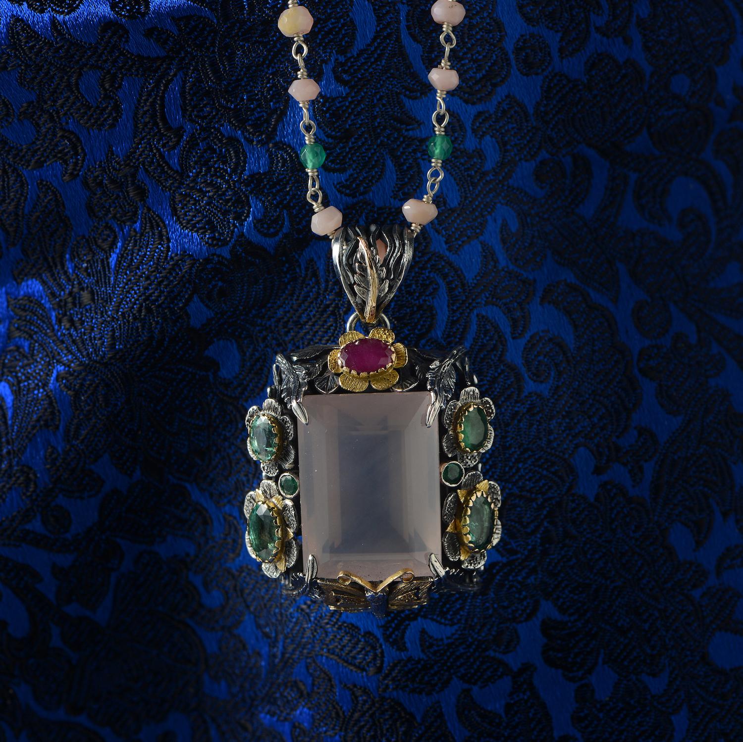 This statement one-of-a-kind pendant has been handmade in our workshops. It features a hand cut central rose quartz, surrounded by emeralds and capped with a ruby. The pendant has hand-engraved flowers, leaf and a butterfly motif on it in 18ct gold