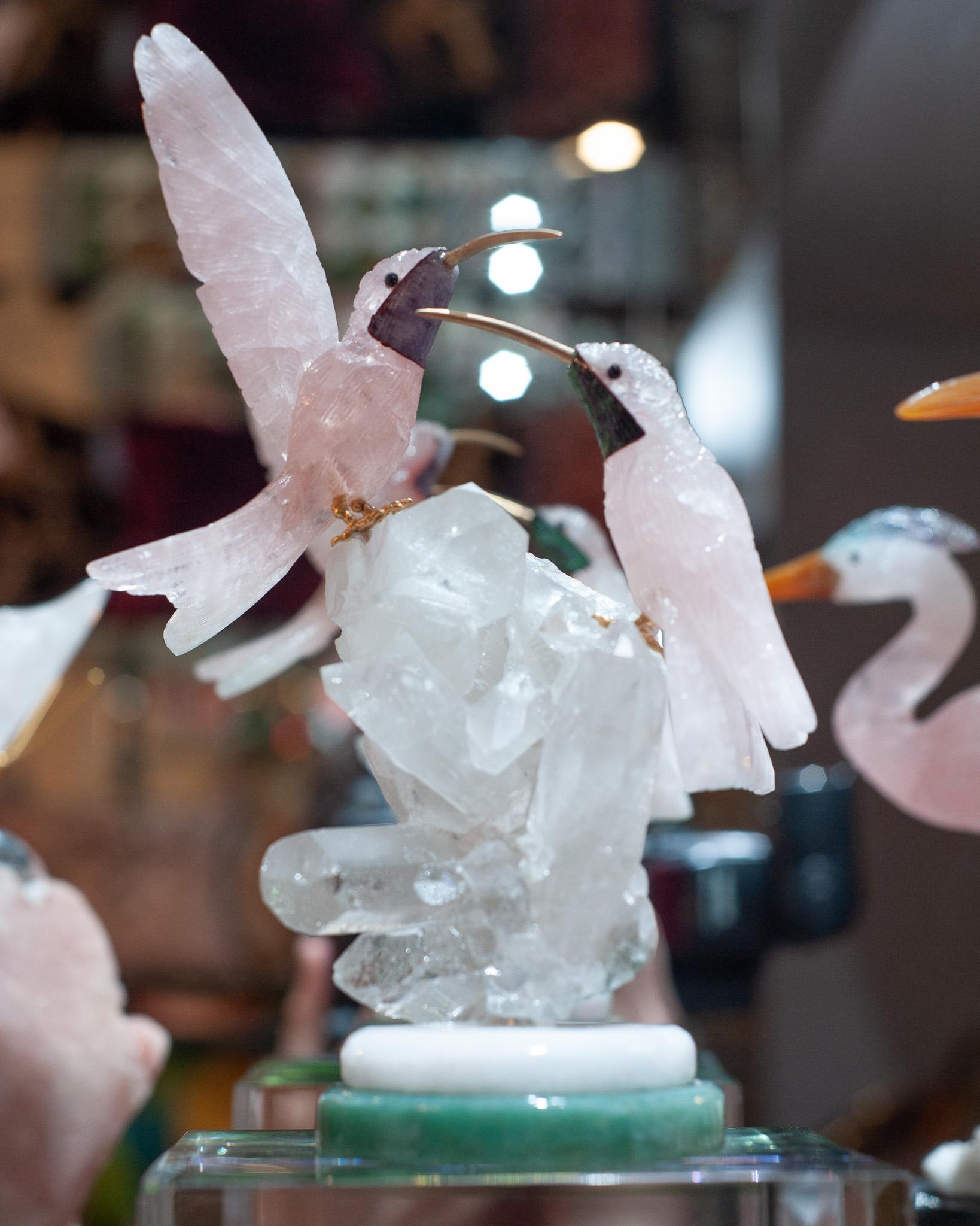 A beautiful hand carved semi precious rose quartz stone hummingbird pair, with brass beak and feet, mounted on a rock crystal quartz and green marble mineral specimen base. This exotic sculpture is a decorative combination of ornithology and geology.