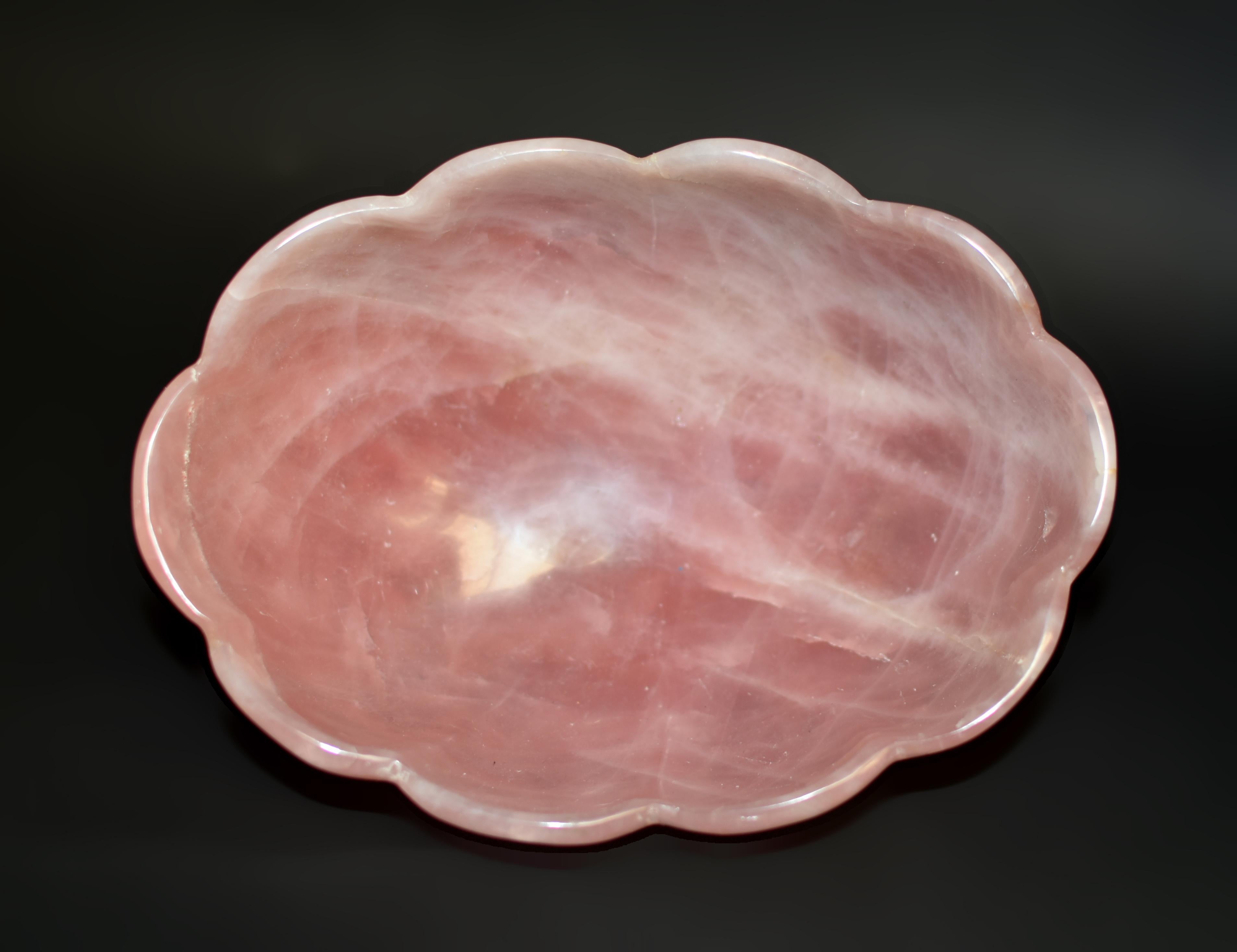 Un grand bol artisanal, taillé dans un énorme morceau de quartz rose, une pierre précieuse naturelle. De forme ovale allongée, sur un pied solide, avec un bord festonné et un corps 