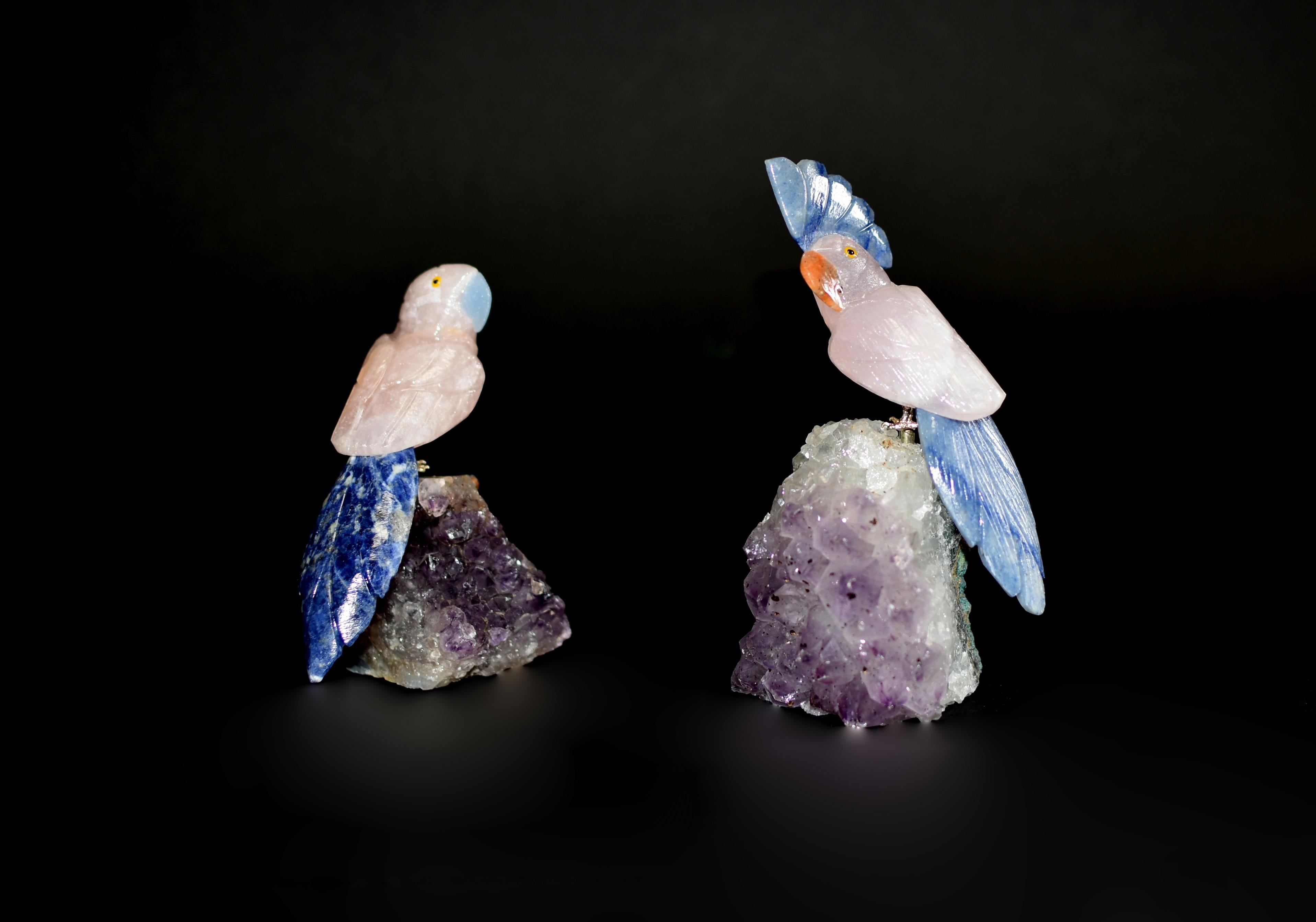 Two rose quartz parrots perched on amethyst clusters. Realistically modelled with curious and amusing expression, with natural rose quartz plumage and blue sodalite tails. Beaks in blue and orange calcite. The claws in brass, mounting on clusters of