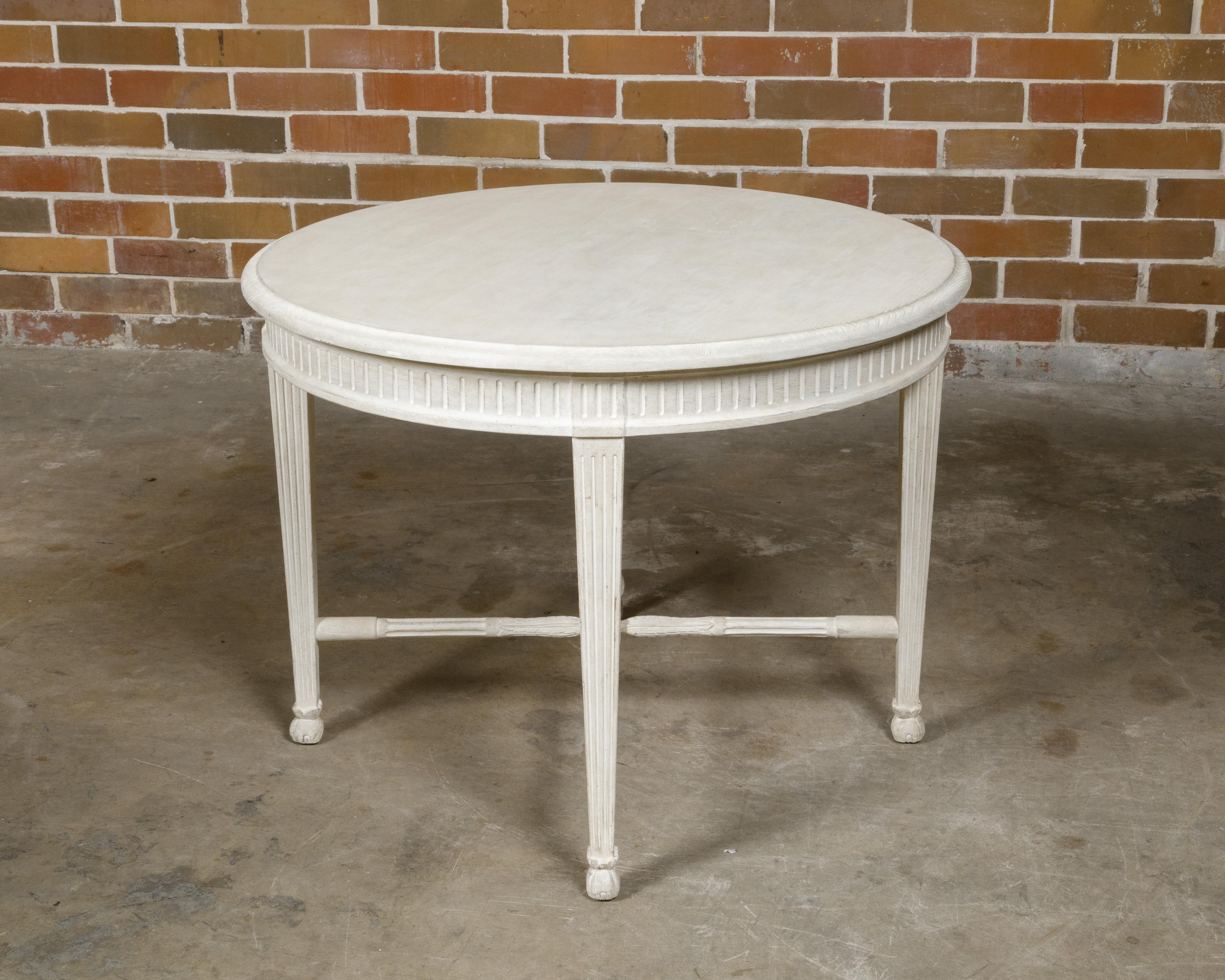 A Rose Tarlow Louis XVI style white painted pine center table from the Midcentury period with round top, fluted apron and legs and X-Form cross stretcher. This elegant Rose Tarlow Louis XVI style center table, crafted from white painted pine,