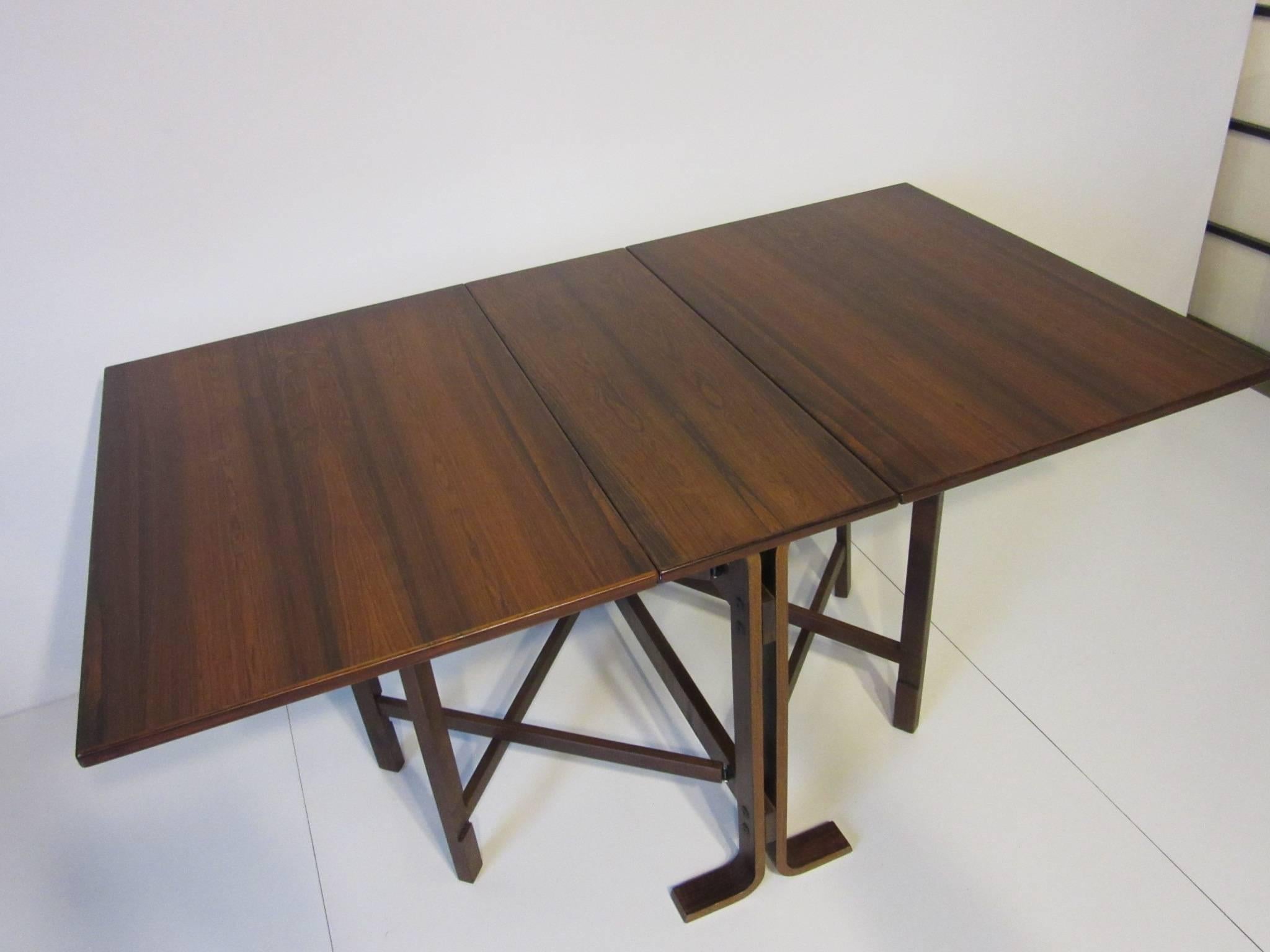 A dark and rich Brazilian rosewood gate leg dining table with two folding leaves which can be fully opened or just one end used. Nice for a small space since the table can be stored or used as a console which when closed measures 11.88 