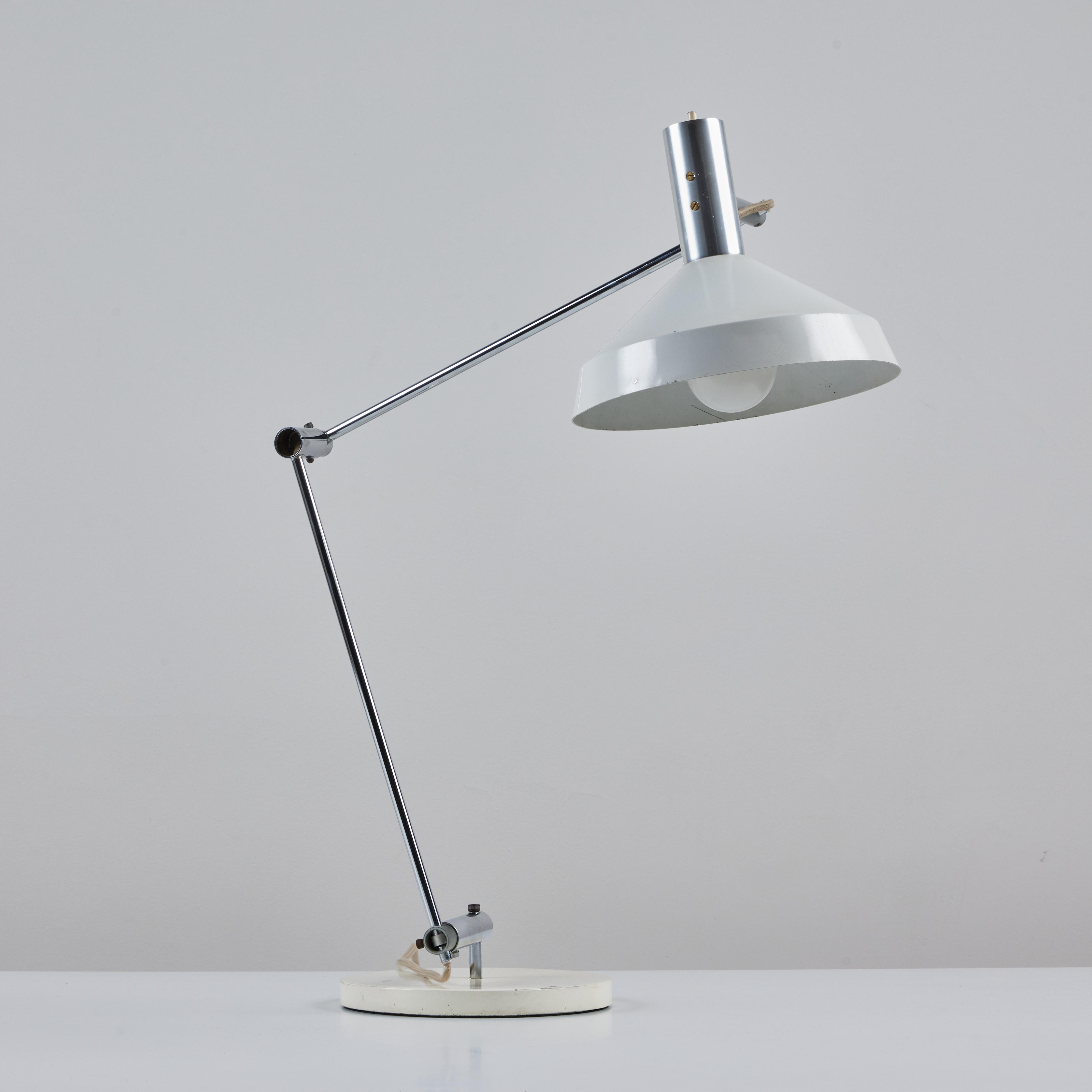 This table lamp comes from the collaboration of Rosemarie & Rico Baltensweiler, c.1960s, Switzerland. The lamp features a white enameled metal base and shade. The chrome plated stem of the lamp articulates while the shade is adjustable allow for