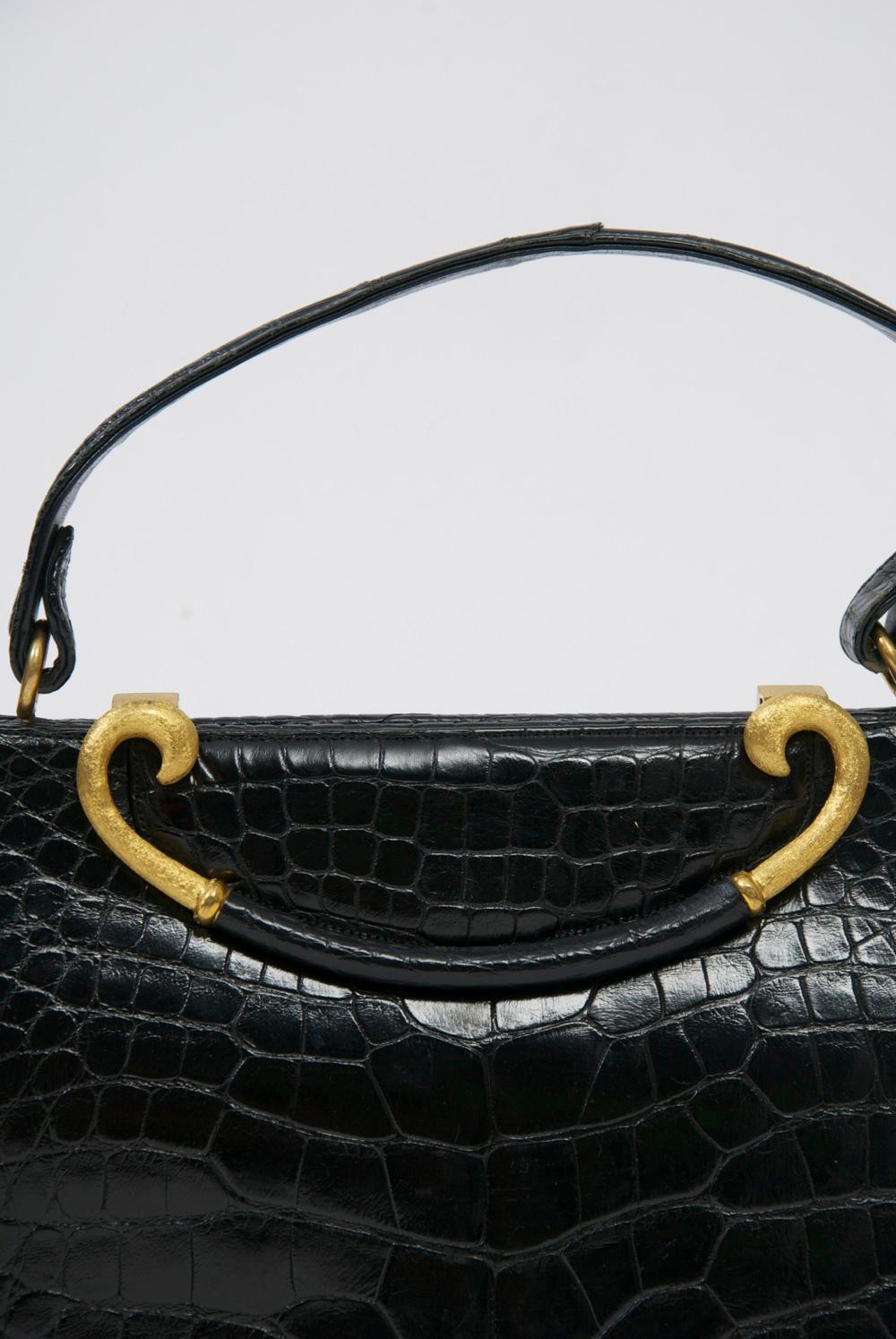 Classic 1960s handbag by Rosenfeld in black leather stamped to resemble alligator, its outstanding feature the curved clasp of brushed goldtone metal with leather center that lifts up to open the bag. The rich interior is of red leather with side