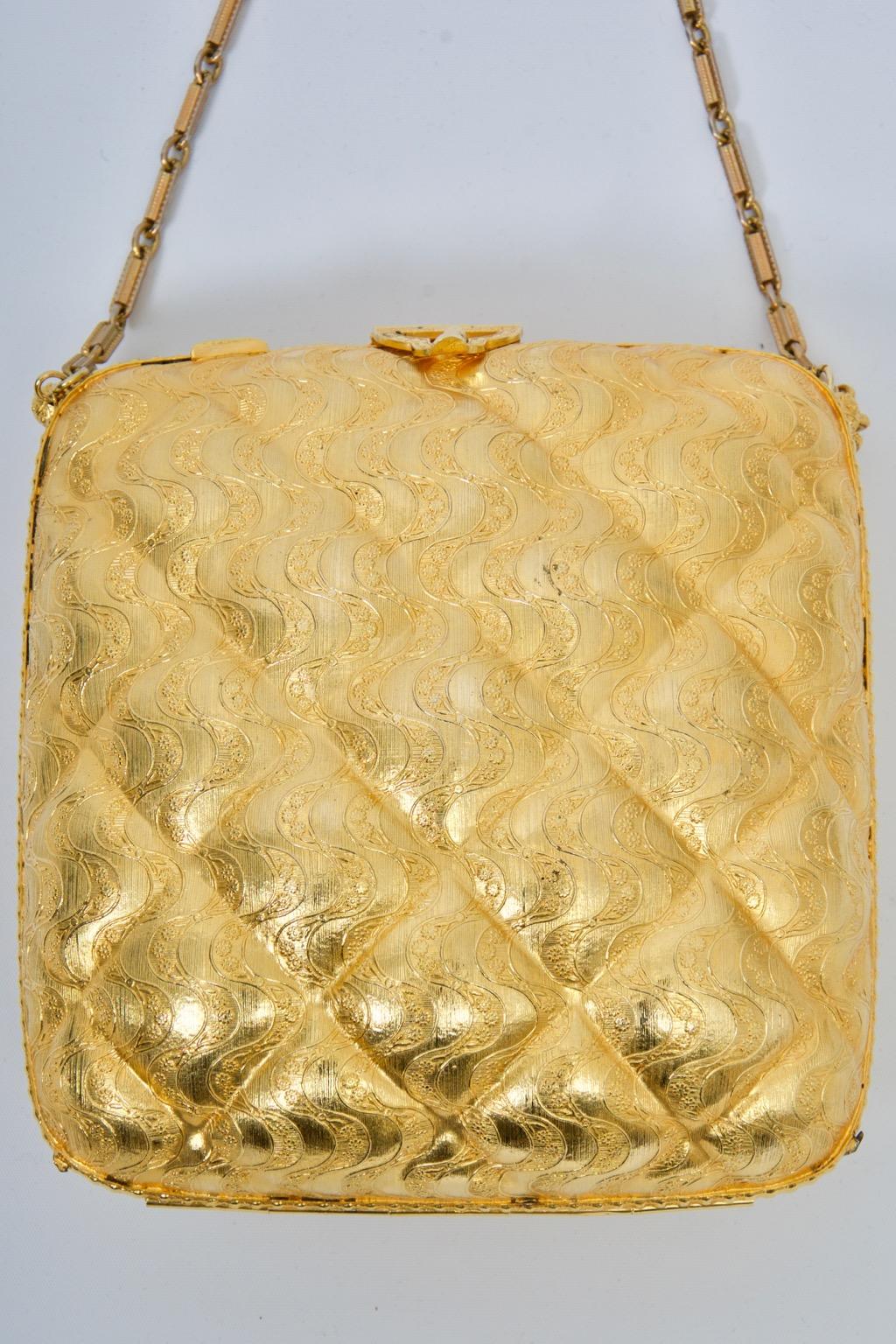 Rosenfeld c.1960s evening bag with chain of gold metal metal molded in a quilted and wave design. A gold metal triangular clasp, echoed on the reverse, secures the bag, while small gold tassels adorn the ends of the chain. Interior is coordinating