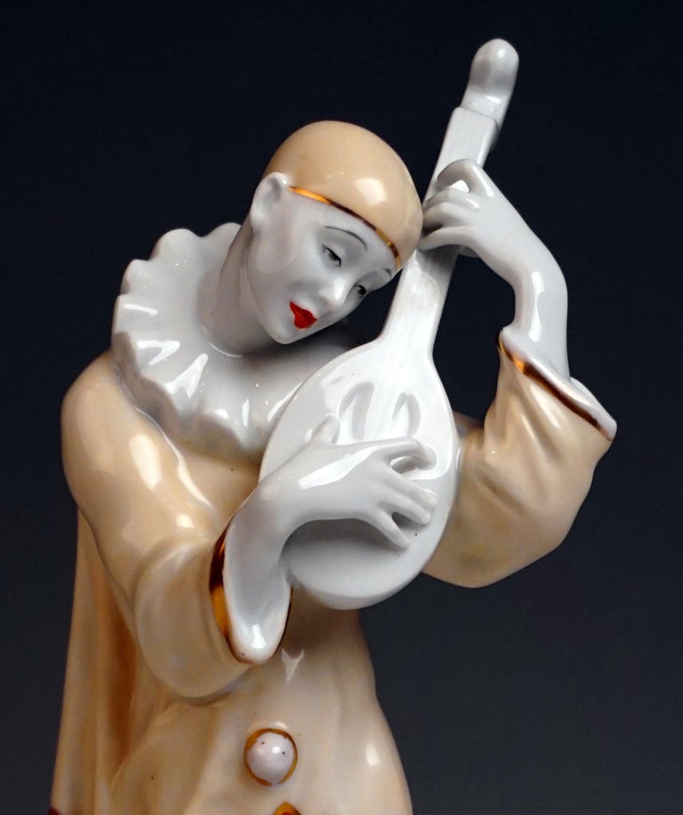 Very rare Art Deco figurine of a lute playing pierrot

In a wide bright robe with Art Deco decoration. Wearing hat and ruff and playing a lute. A white cat snuggles up his legs. The group of figures is based on a graduated round base with golden