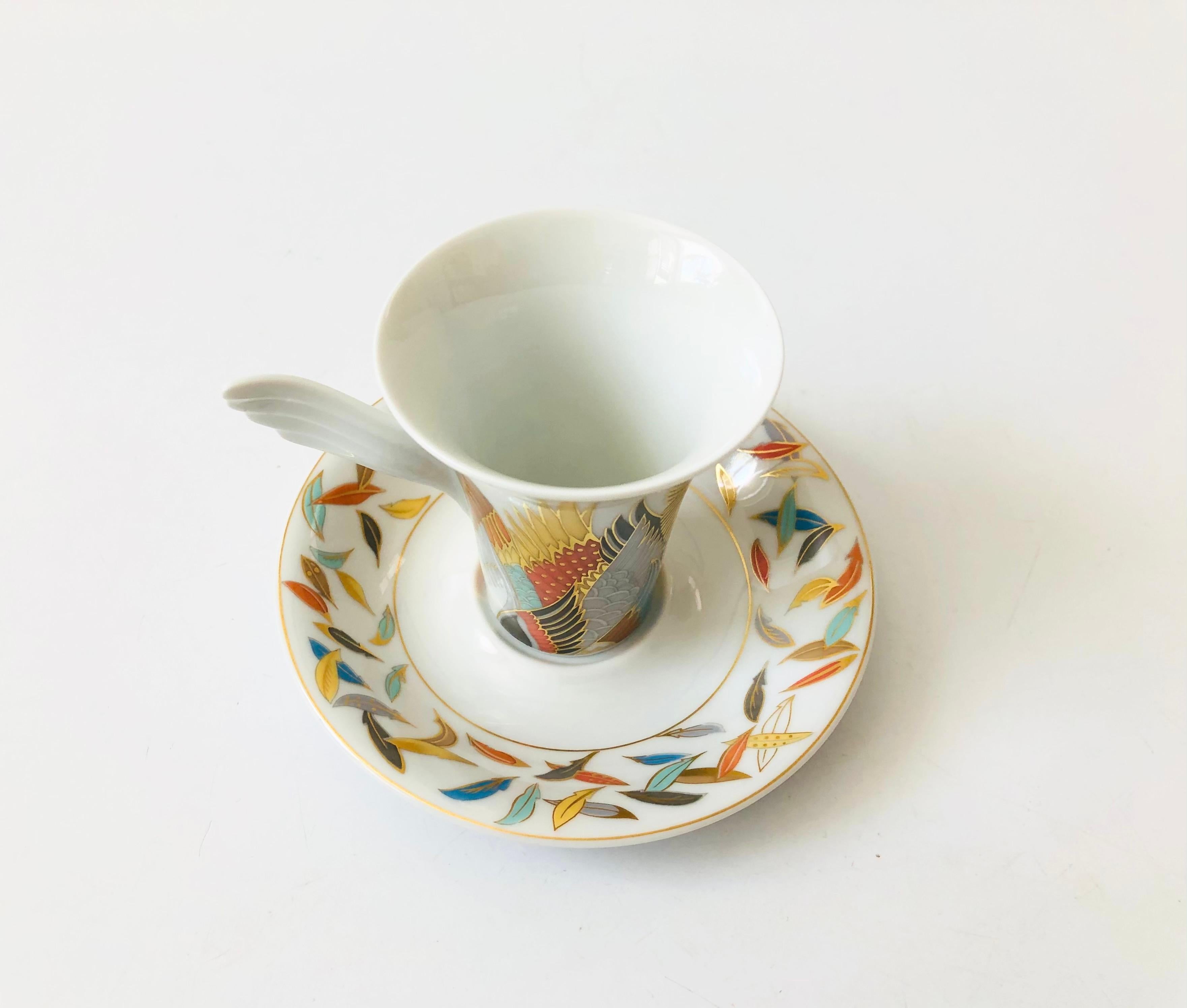 A vintage collectible porcelain espresso mug and saucer set from the Mythos line by Rosenthal, Germany. Signed by the designer, Jane Osborn Smith, and numbered NR 6. Features an intricate matching design on the cup and saucer with a winged handle.