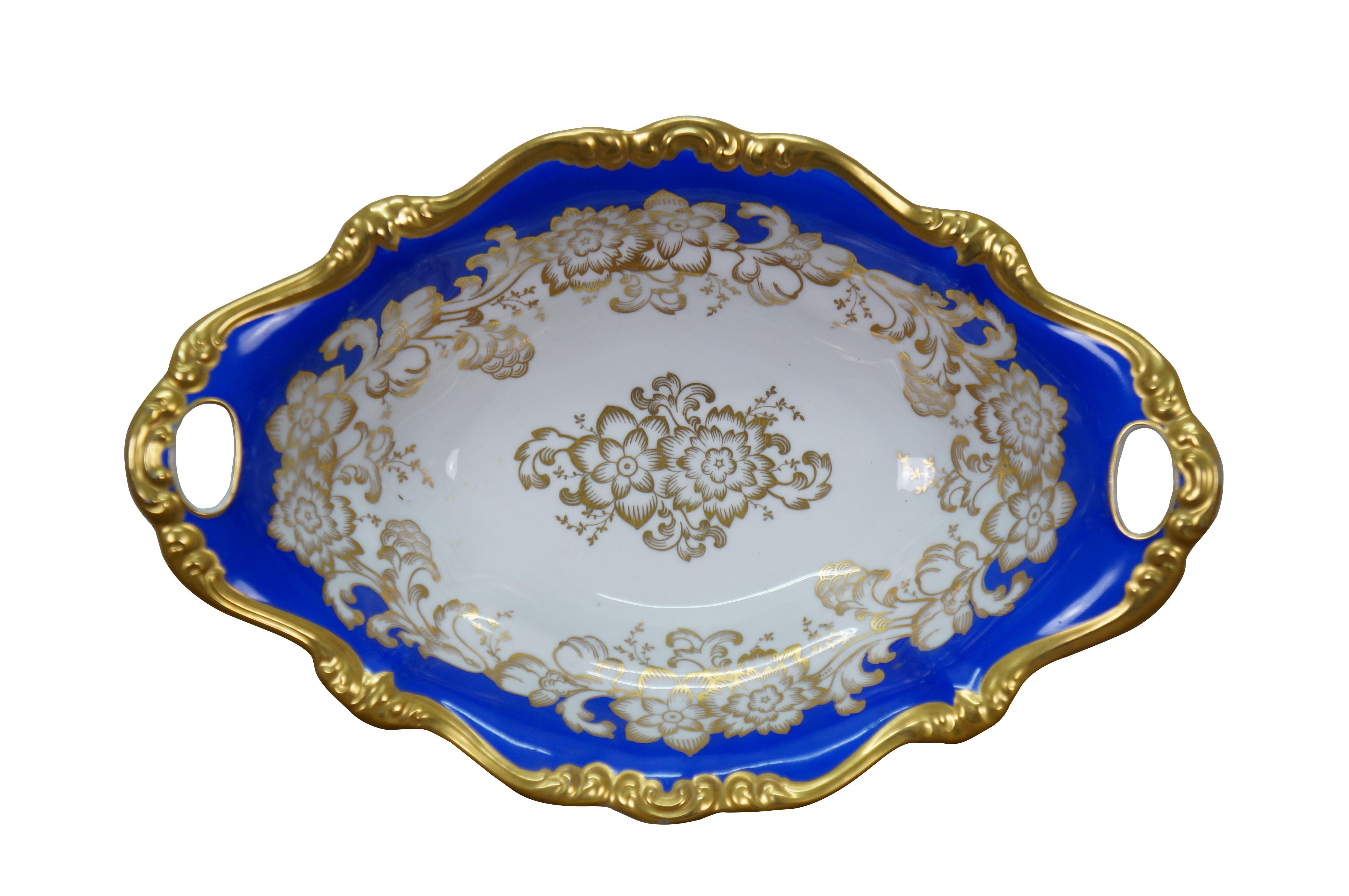 1933 Rosenthal Pompadour porcelain centerpiece /  serving dish. Oval shape with scalloped edge, footed base, pierced handles, decorated with gilt flowers and trim around a deep blue border.

Dimensions:
13.75