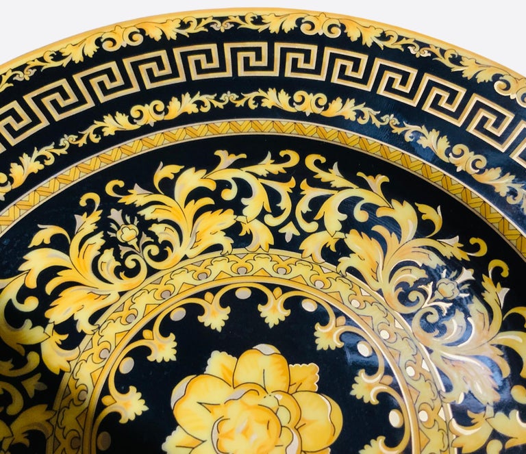 This is a Rosenthal porcelain designed by Versace, “Floralia Gold”, bread and butter/wall decor plate. It is hand painted black in the background with a bright yellow Ikarus flower in the center. The flower is surrounded by a gilt yellow garland of