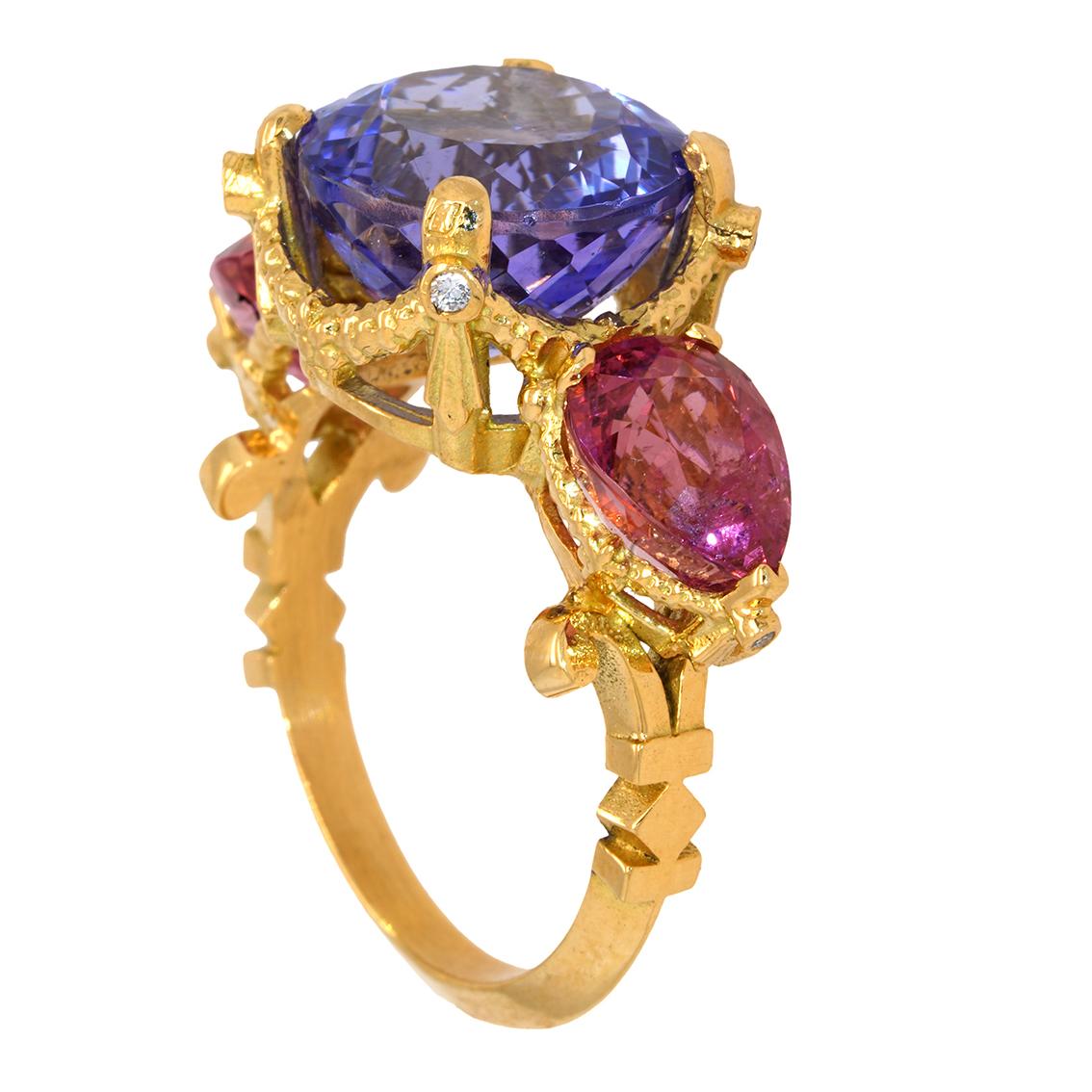 Intricately handcrafted in 18kt yellow gold this exquisite ring features a breathtaking round rich blue violet colored tanzanite aloft a signature William Llewellyn Griffiths garland setting studded with four 1.4mm round brilliant cut white