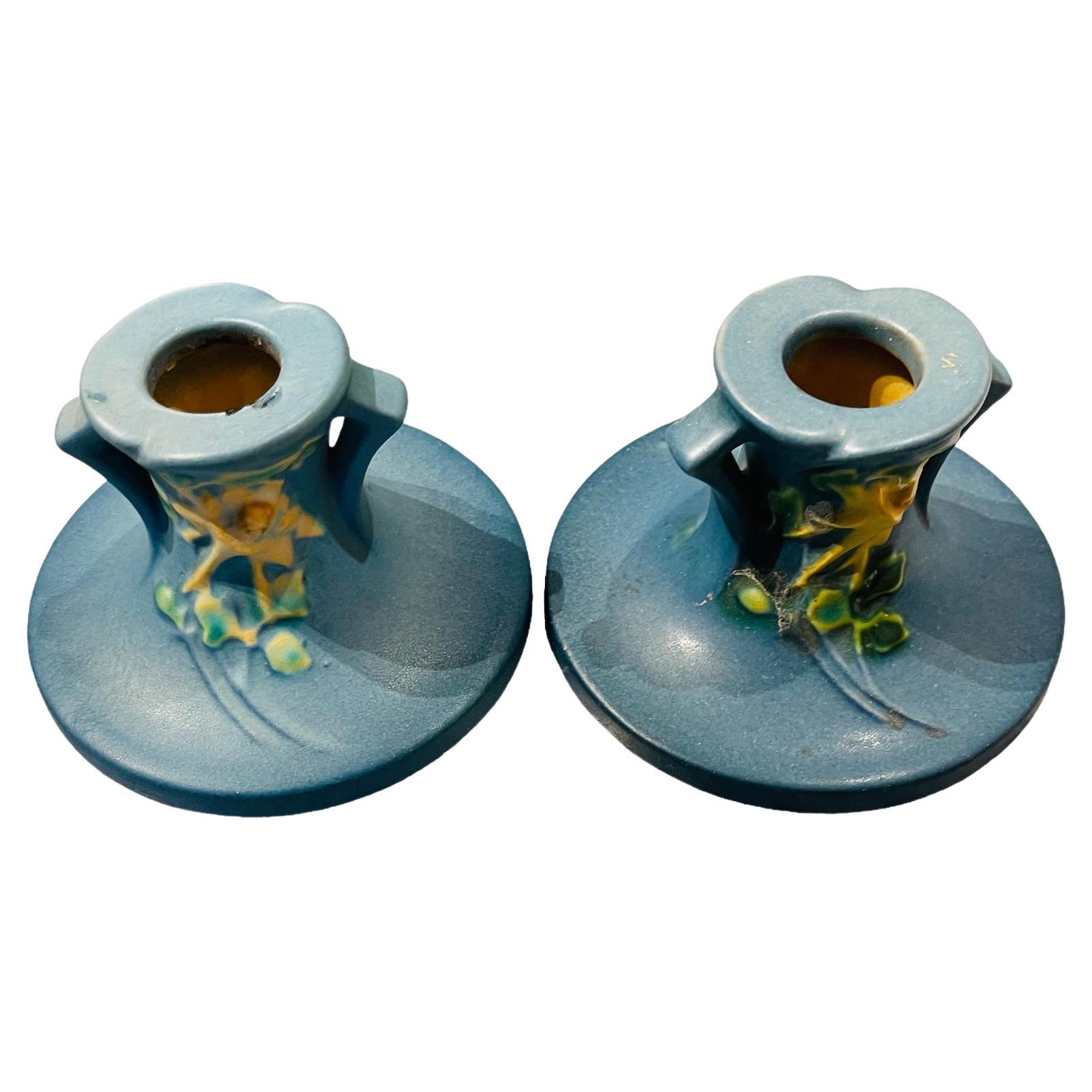 This is a Roseville Art Pottery Columbine pattern pair of candleholders. They are blue and adorned with a branch of yellow Columbine flowers and green/yellow leaves in the front. Below their base are hallmarked Roseville with the mold number 1145-2