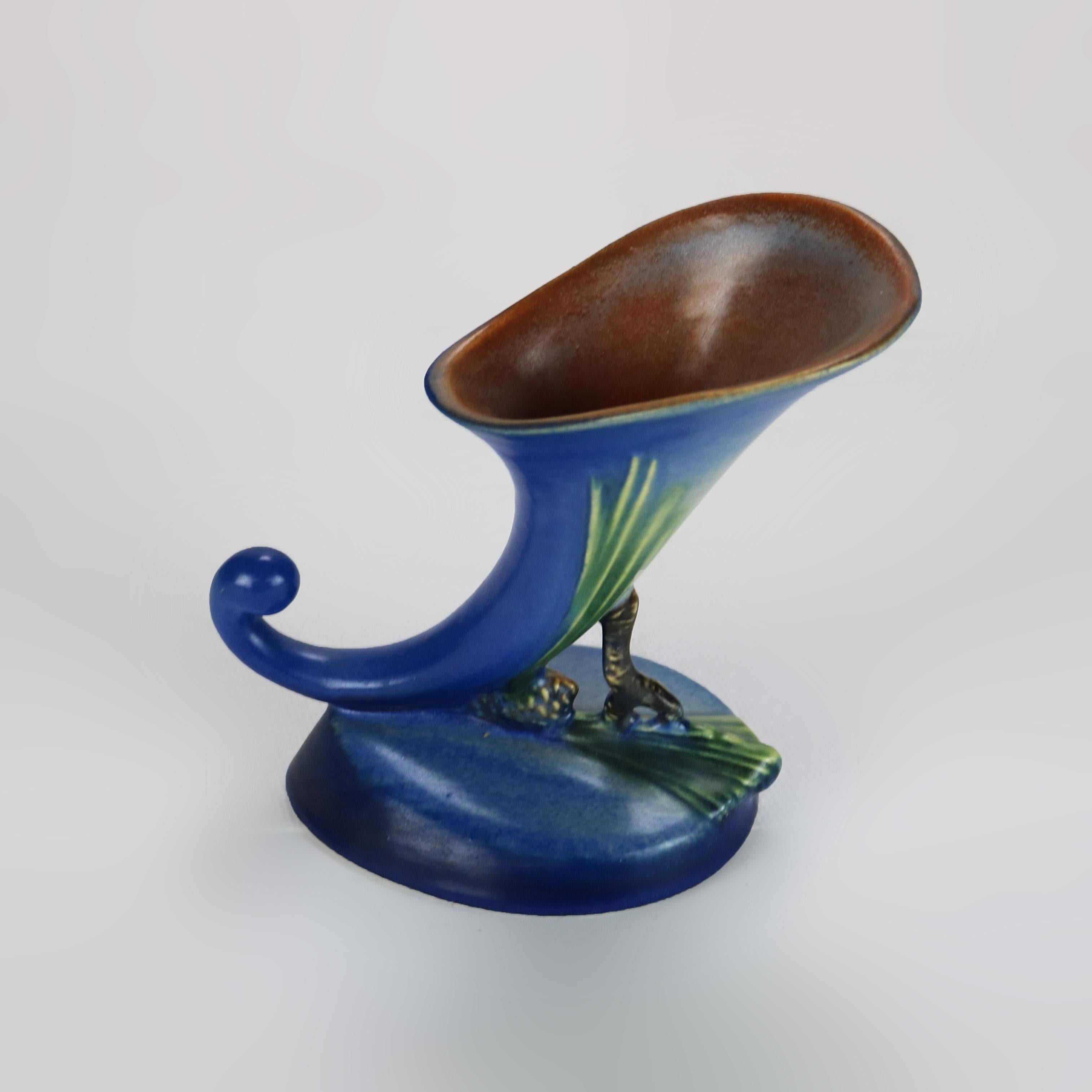 Roseville Art Pottery Dark Blue Cornucopia Vase With Pinecone Pattern Mid 20thC

A beautiful example of Roseville Art Pottery, this dark blue cornucopia vase features a striking pinecone pattern. The vase showcases the classic Roseville style with
