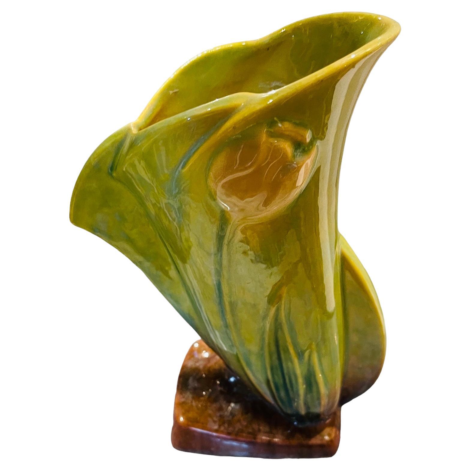 This is a Roseville Art Pottery Wincraft green yellow tulip vase. The vase is shaped like a flower bud that its petals are starting to open. It is decorated with a relief of large green/yellow leaves & light pink tulip flowers. The upper border is