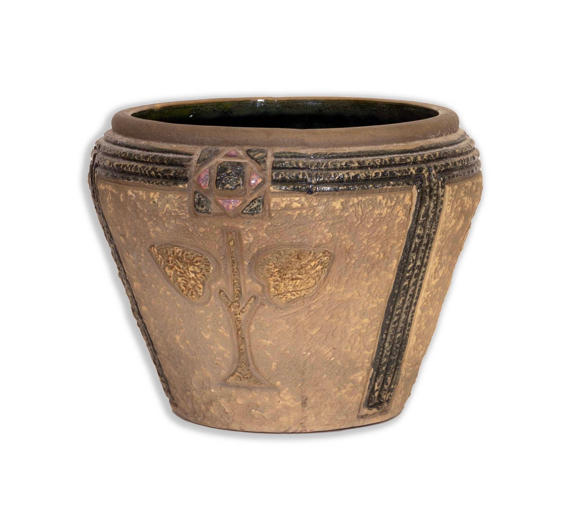 Distinctive and elegant, this Roseville Mostique Large Jardiniere Planter from the early 20th century embodies the charm of the Arts and Crafts movement. Featuring intricate, textured motifs in earthy tones with touches of pink and black, this