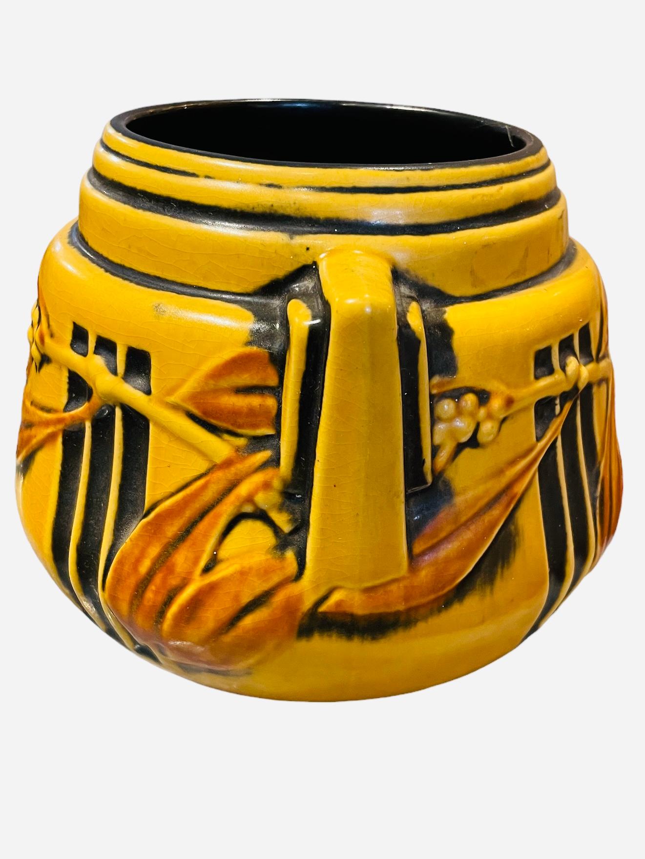 This is a Roseville Pottery Laurel pattern round shaped vase. The vase has a yellow color background decorated with black wide vertical bands. It is also adorned with a relief of Laurel brown leaves branches in the back and front. Two ninety degree