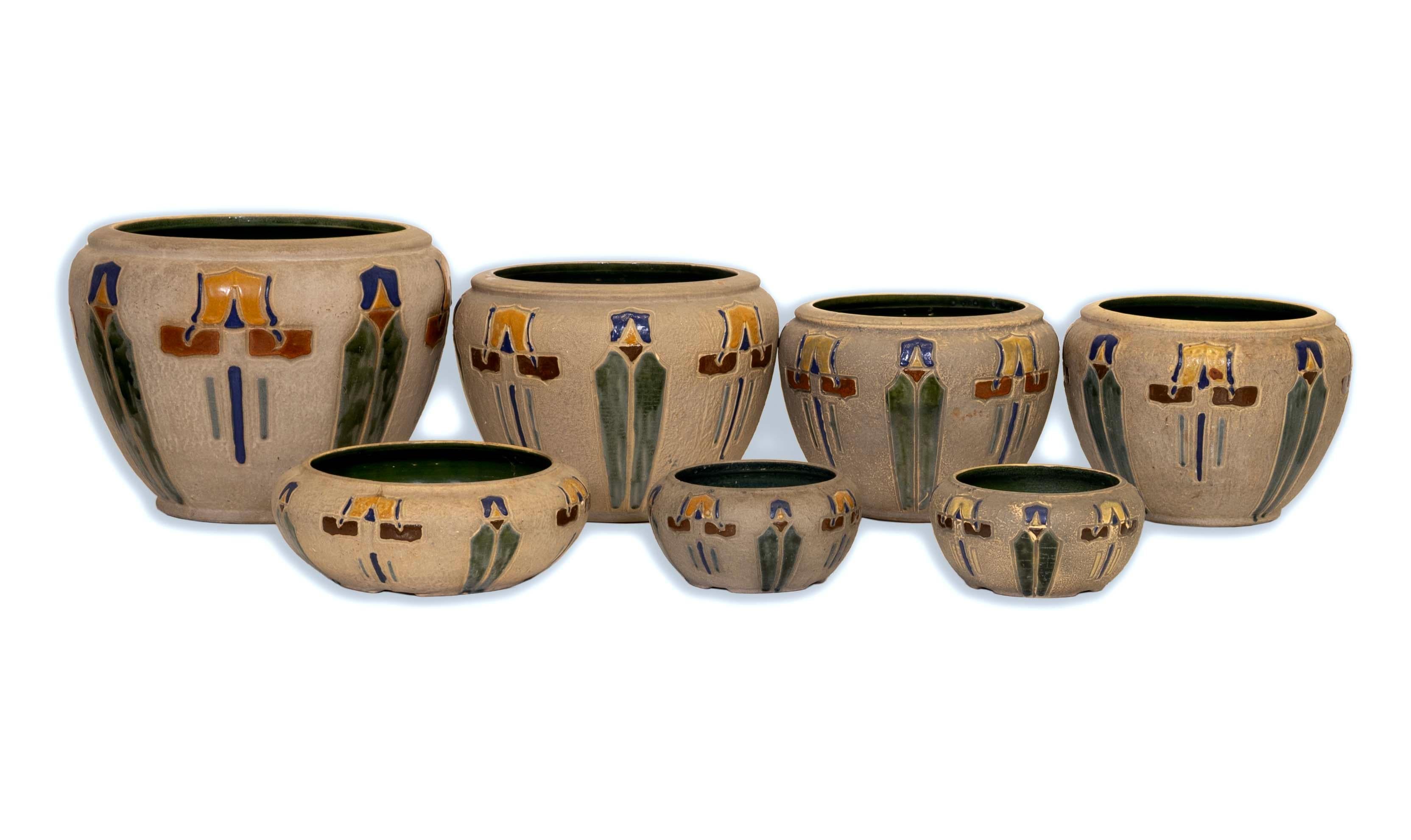 Beautiful and rare, this Roseville Set of 7 Ceramic Mostique Vessels from the early 20th century is a captivating representation of Arts and Crafts design. Each vessel features striking geometric patterns in vibrant shades of yellow, green, blue,