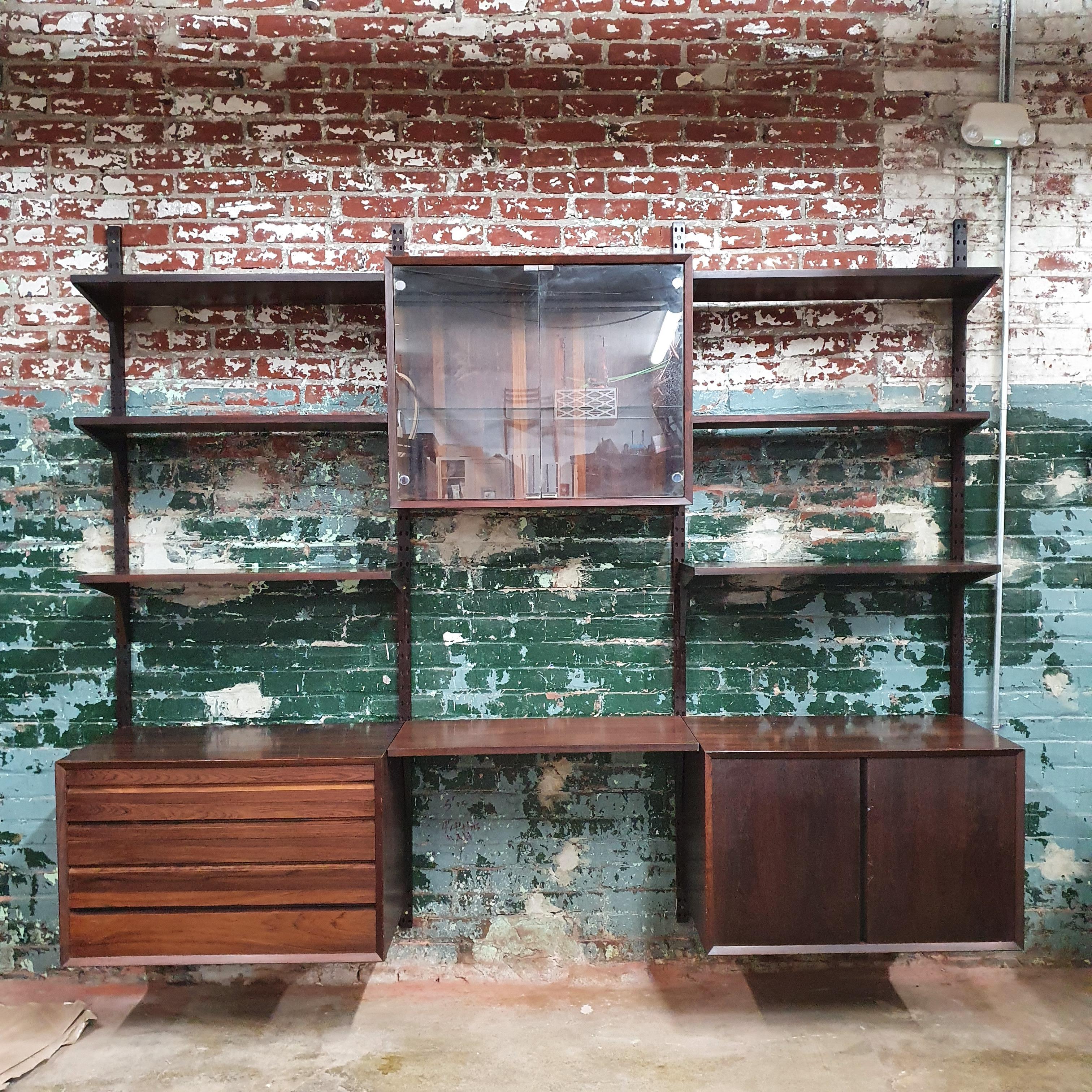 Beautiful rosewood wall unit by Poul Cadovius. 3 bays. 1 4 drawer cabinet, 1 door cabinet with a shelf, 1 glass cabinet with 1 glass shelf. 5 10 inch shelves and 1 8 inch shelf. 4 uprights and corresponding boomerang shelf brackets.