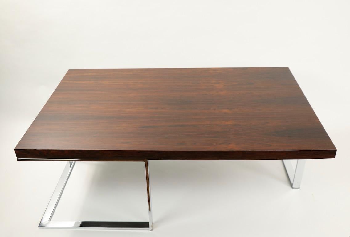 Chic and sophisticated rectangular coffee table having a thick rosewood (veneer) on opposing cantilevered chrome legs. This example is in good, original condition showing some signs of wear and use. Specific condition as follows: inconsequential